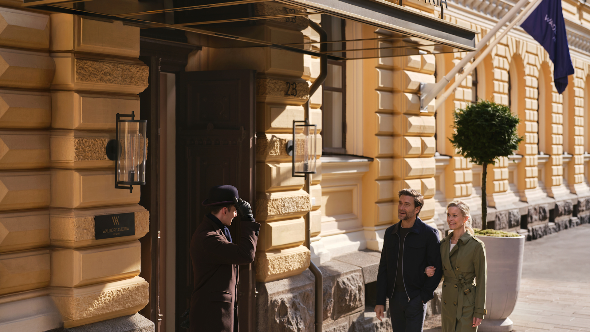 Couple walking into front entrance of the hotel as doorman tips hat