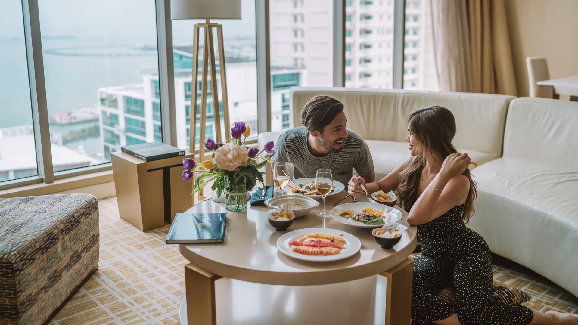 Man and Woman Talking over Dinner at a Coffee Table Near Large Windows