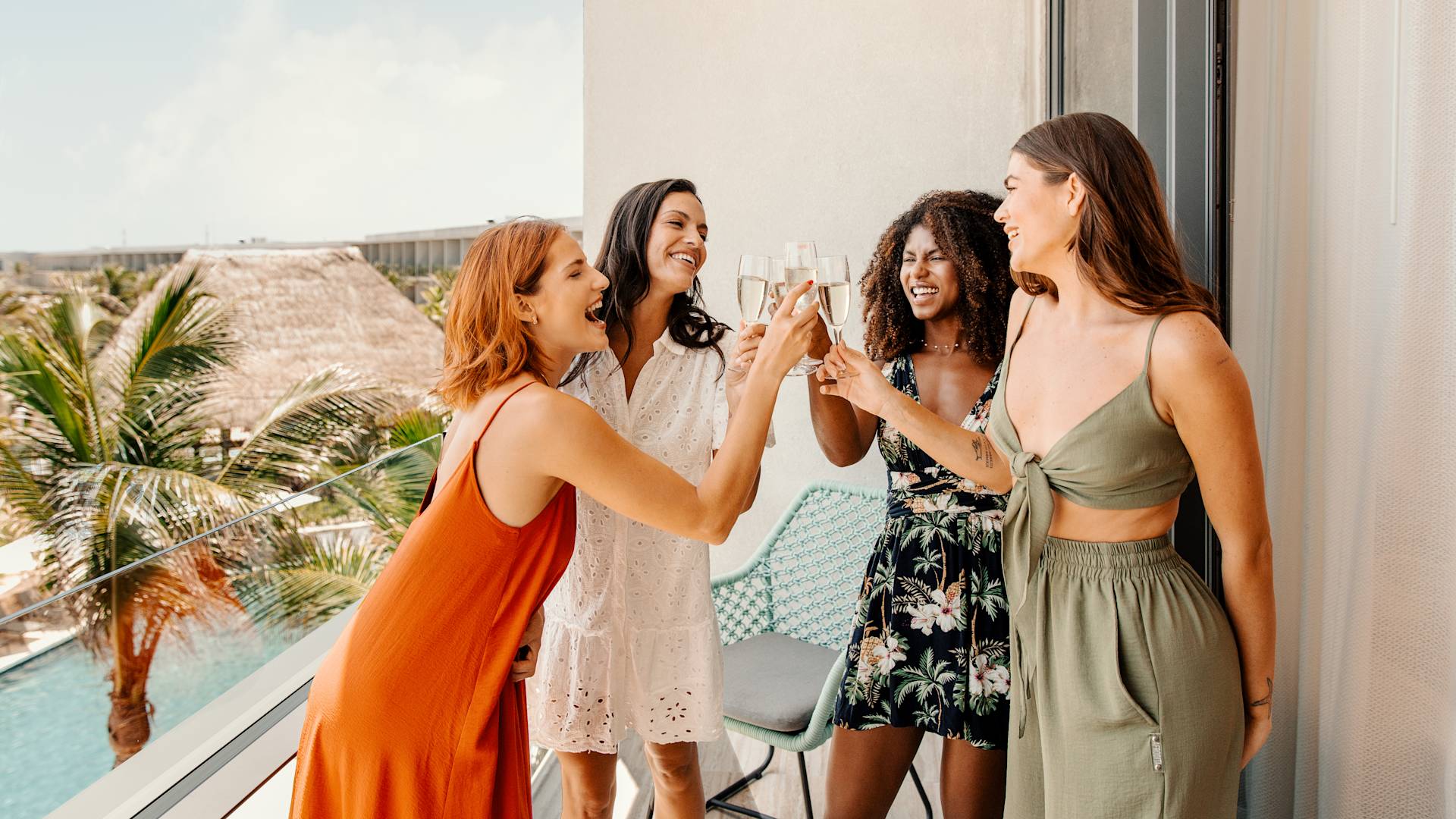 A group of four women raise a drink together on a hotel balcony