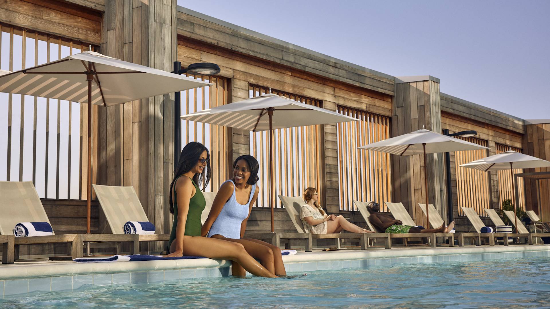 Two woman relaxing by the side of the pool, with legs in the water