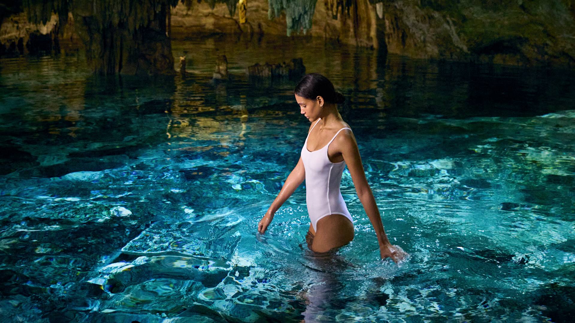 Wanita berdiri di kolam renang bawah tanah, dengan cahaya yang retak di atas batu