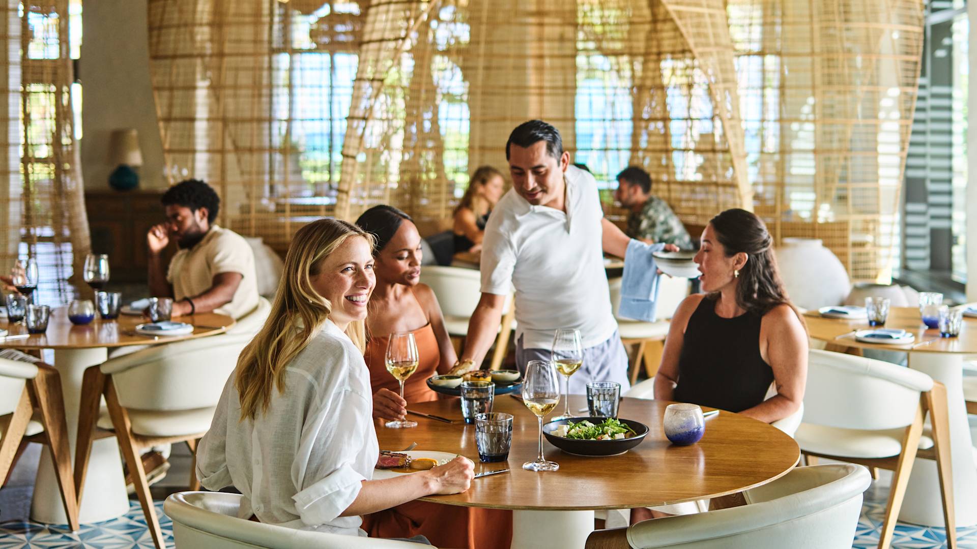 Grup de persoane care iau masa în zona restaurantului. Un membru al personalului servește mâncare