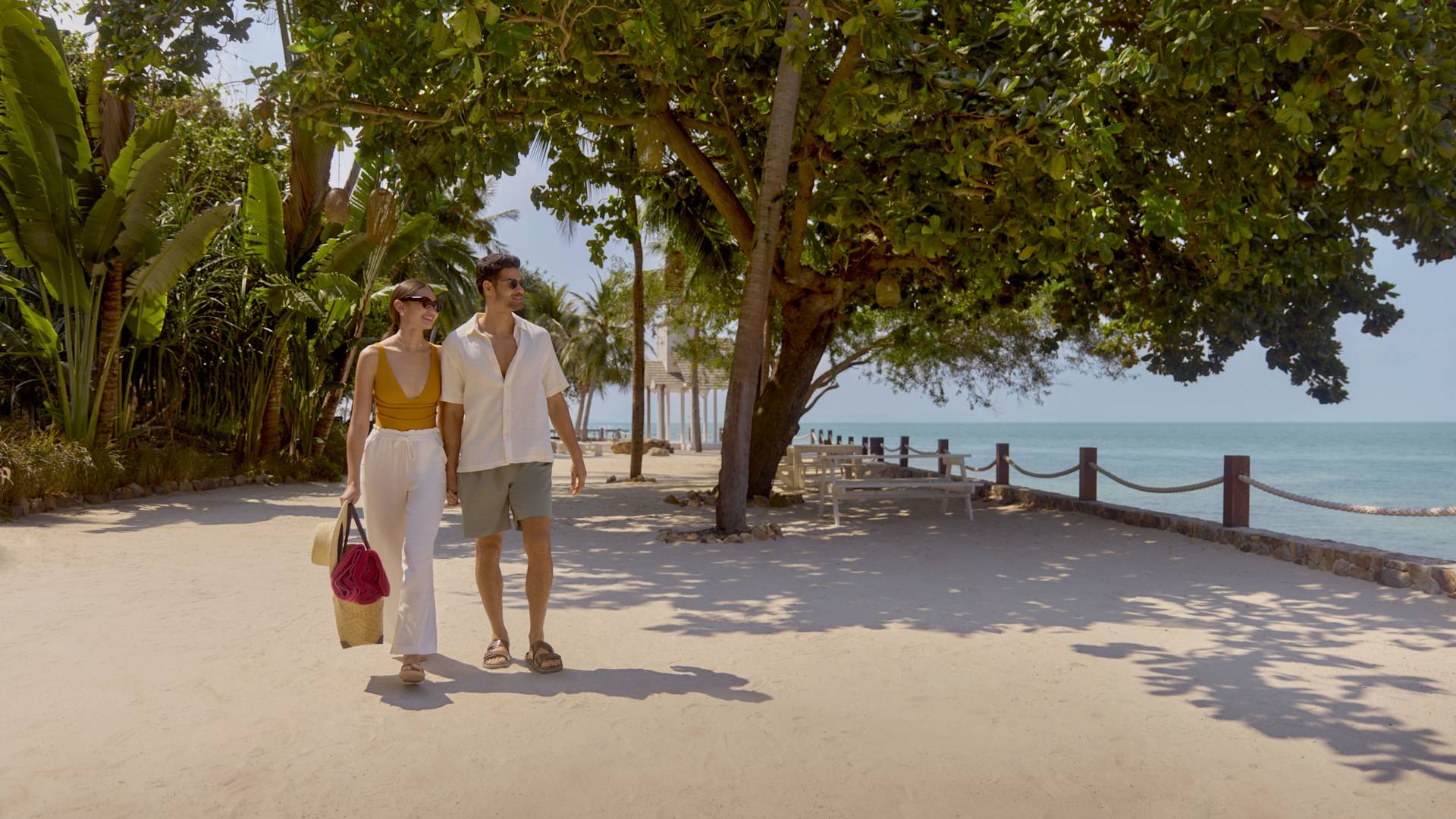 Mann und Frau beim Strandspaziergang mit Blick auf Bäume und Meer