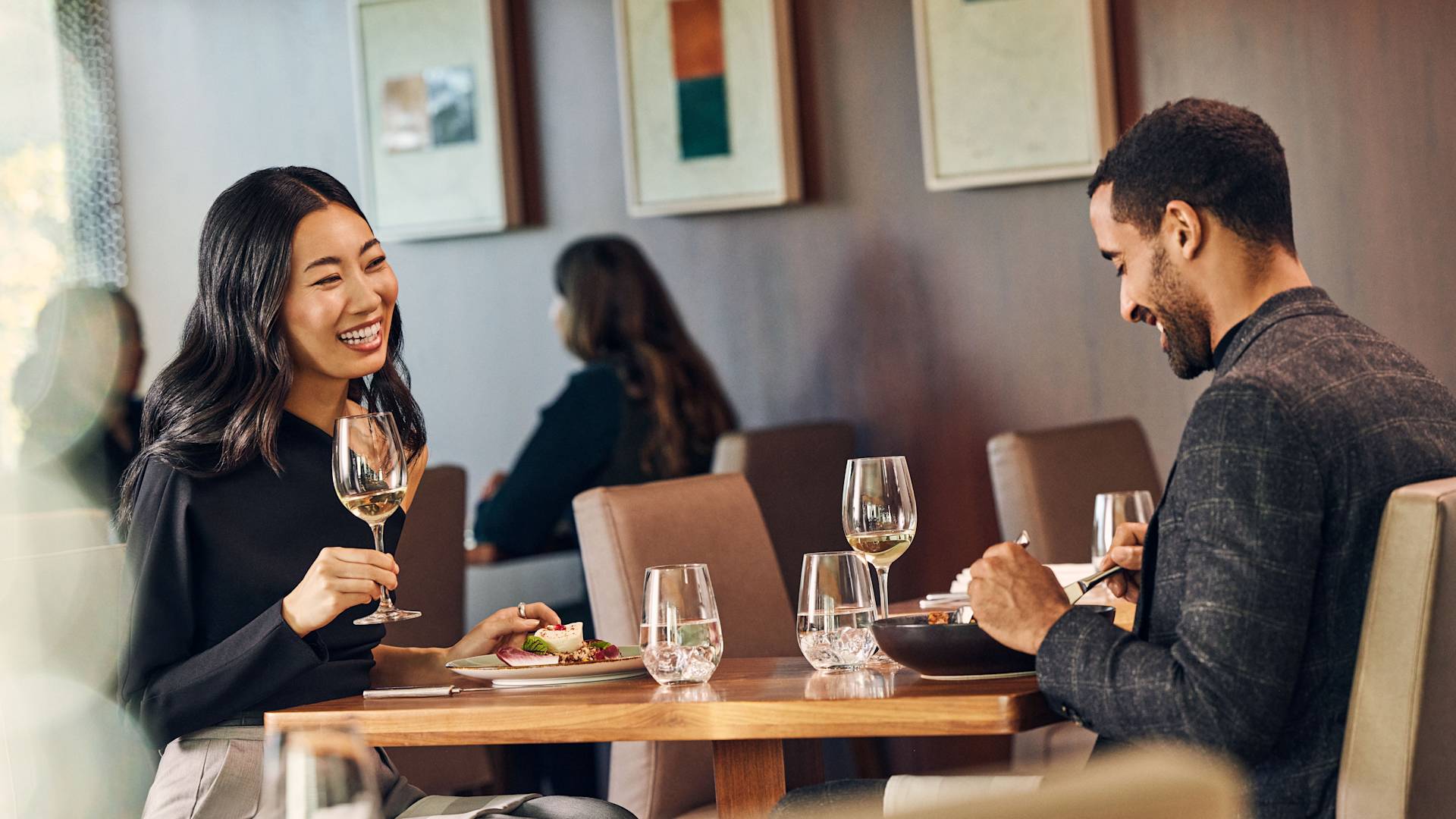 Man and woman smiling as they sit in restaurant area with food and drinks
