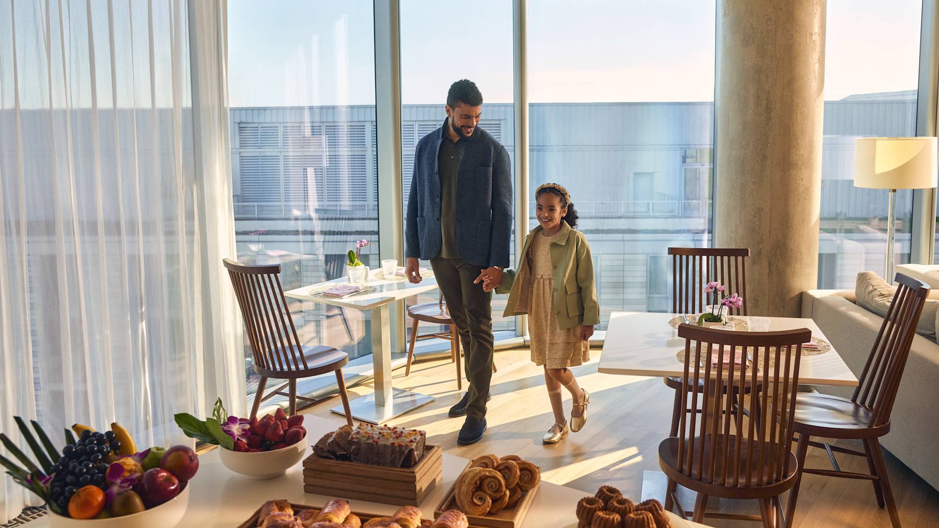 Mann geht Hand in Hand mit jungem Mädchen zum Tisch mit Gebäck und Obst