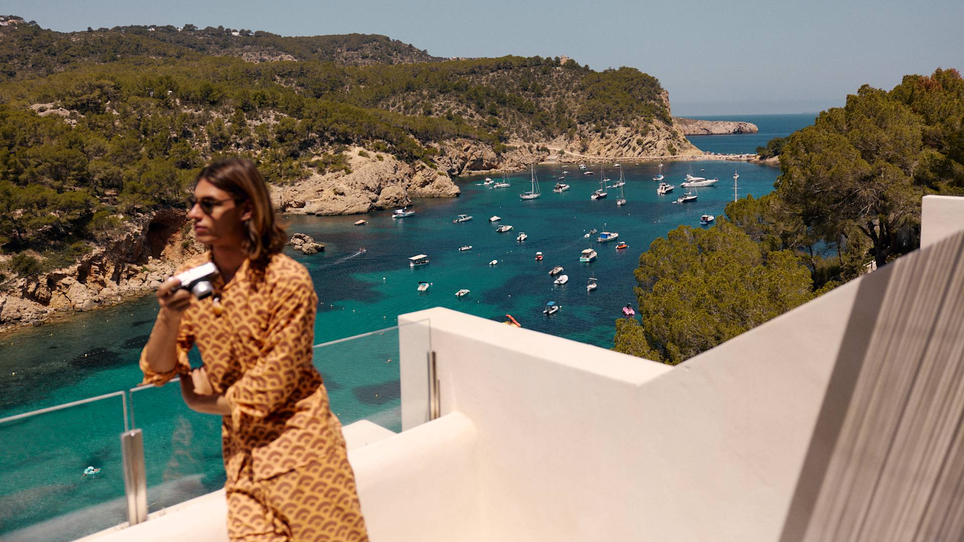 Persona in piedi sul balcone che tiene la camera, con vista sulla baia e sulle barche
