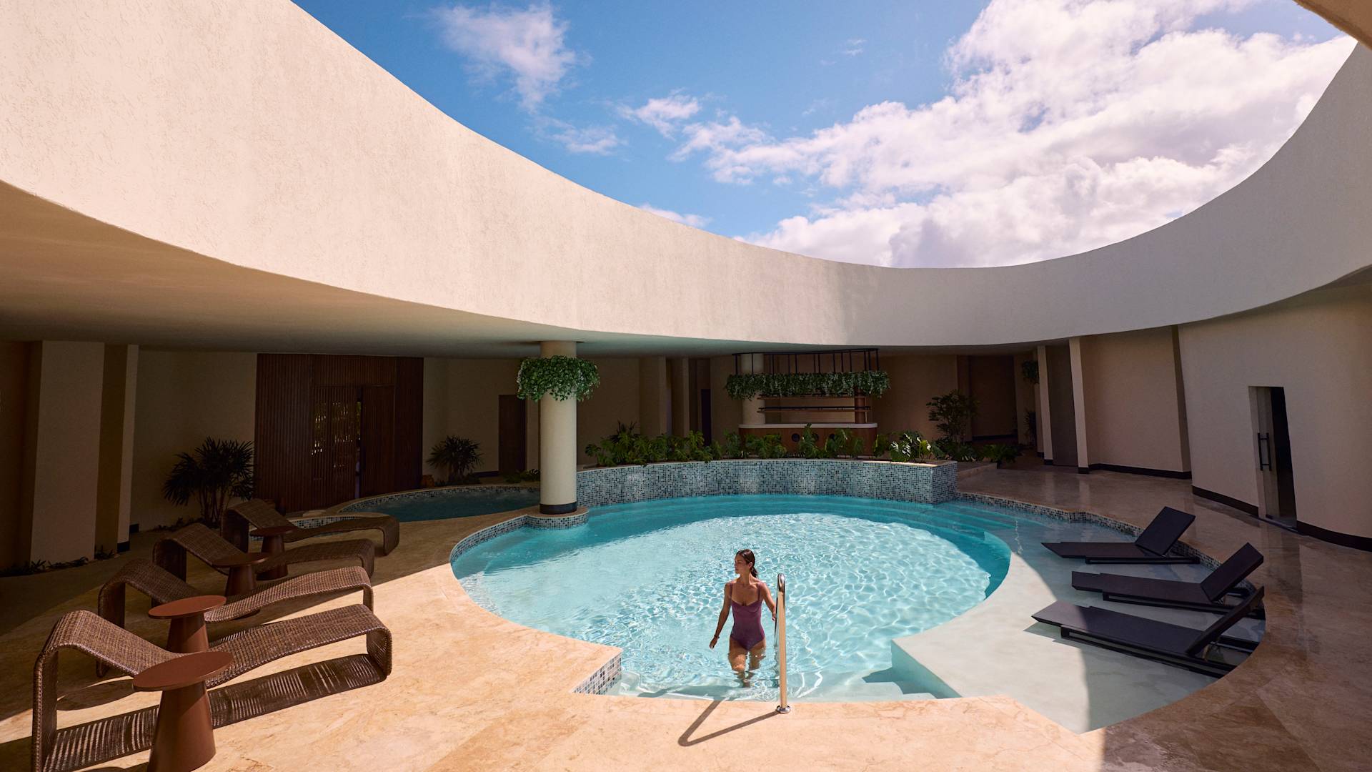 Persoană ieșind dintr-o piscină circulară sub un luminator deschis, înconjurată de arhitectură curbată, scaune lounge și cer albastru strălucitor.