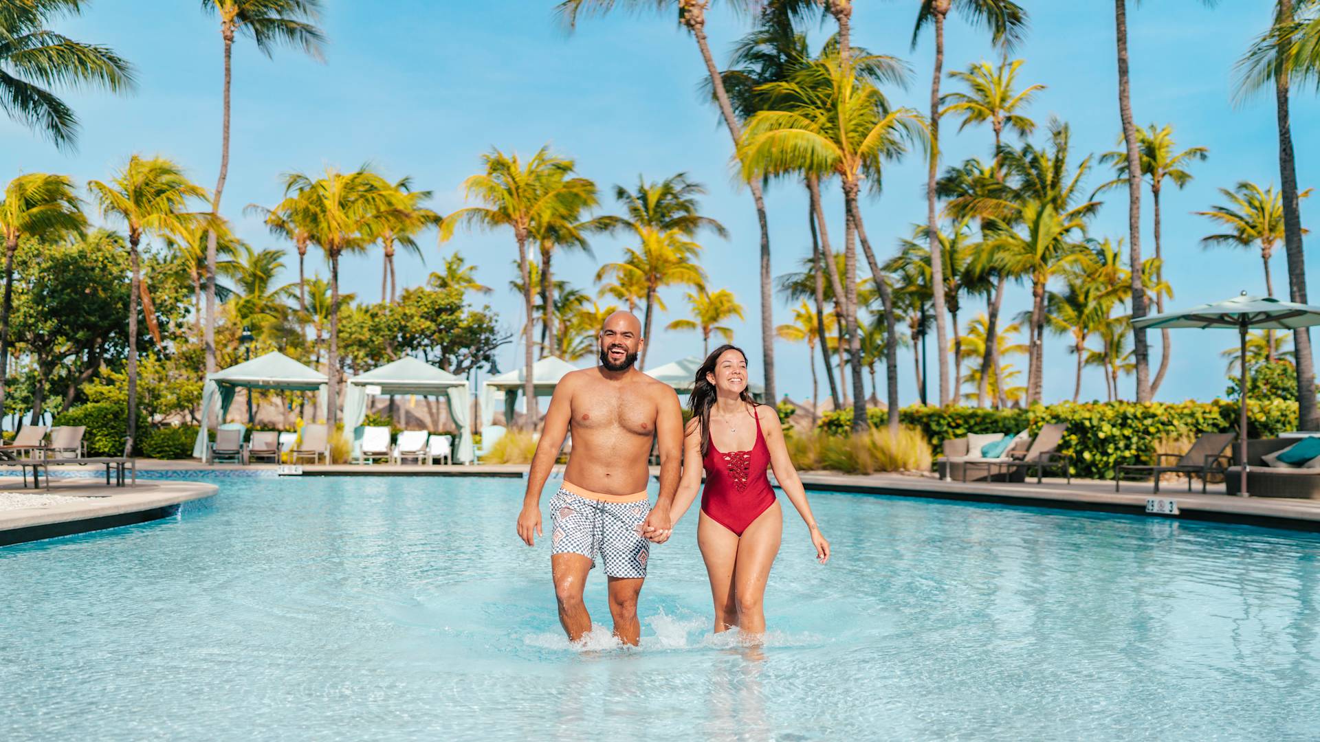 couple in a swimming pool area with palm trees and lounge chairs