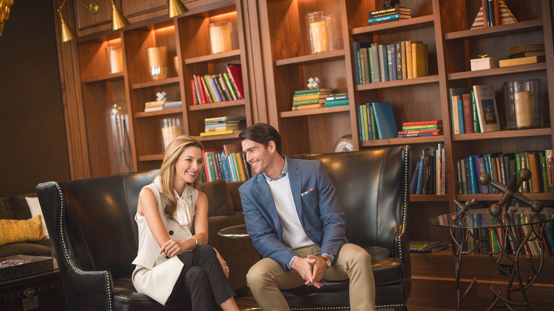a couple sitting and talking in a room with books