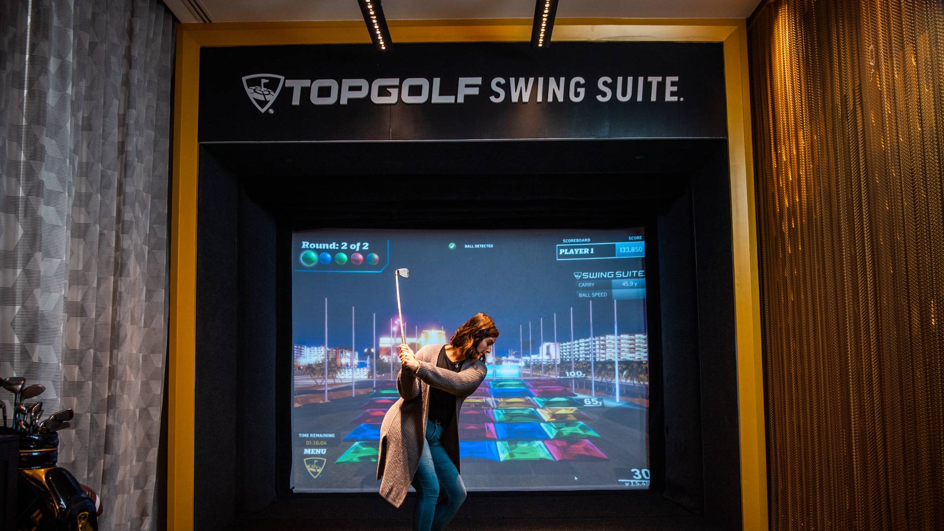 Woman playing virtual golf. The club is raised behind her to start her swing