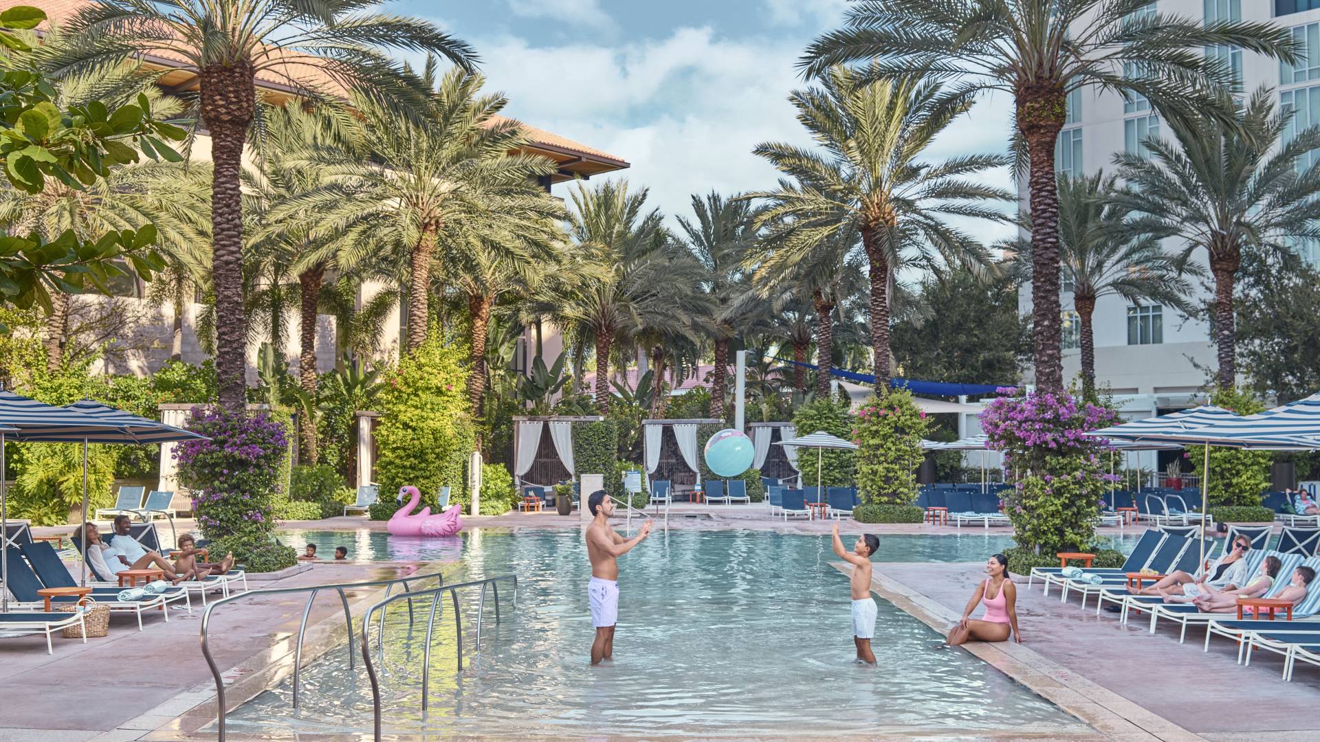 People Playing and Enjoying an Outdoor Pool Area with Lounge Chairs and Palm Trees