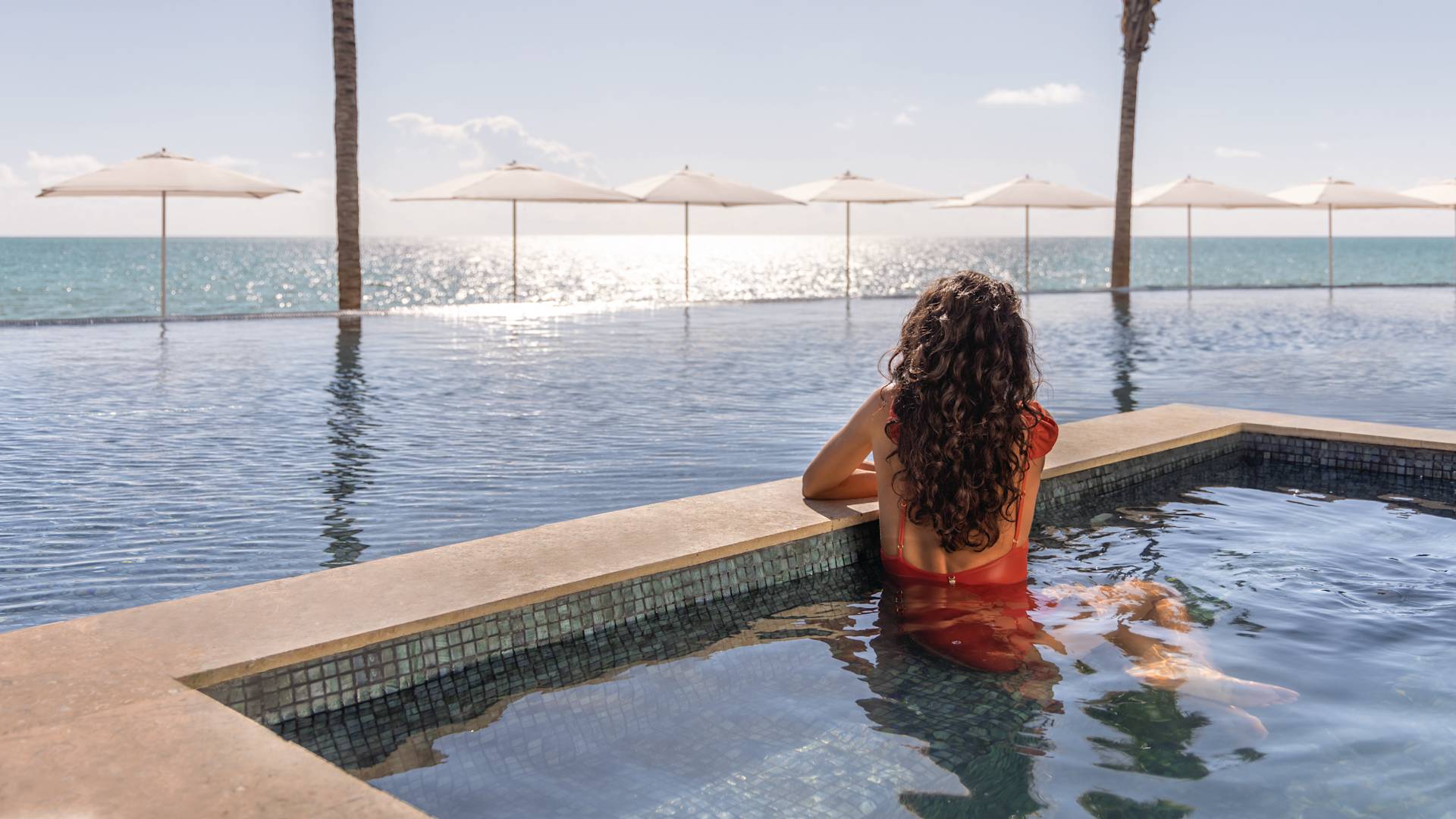 Woman looks out from pool towards ocean