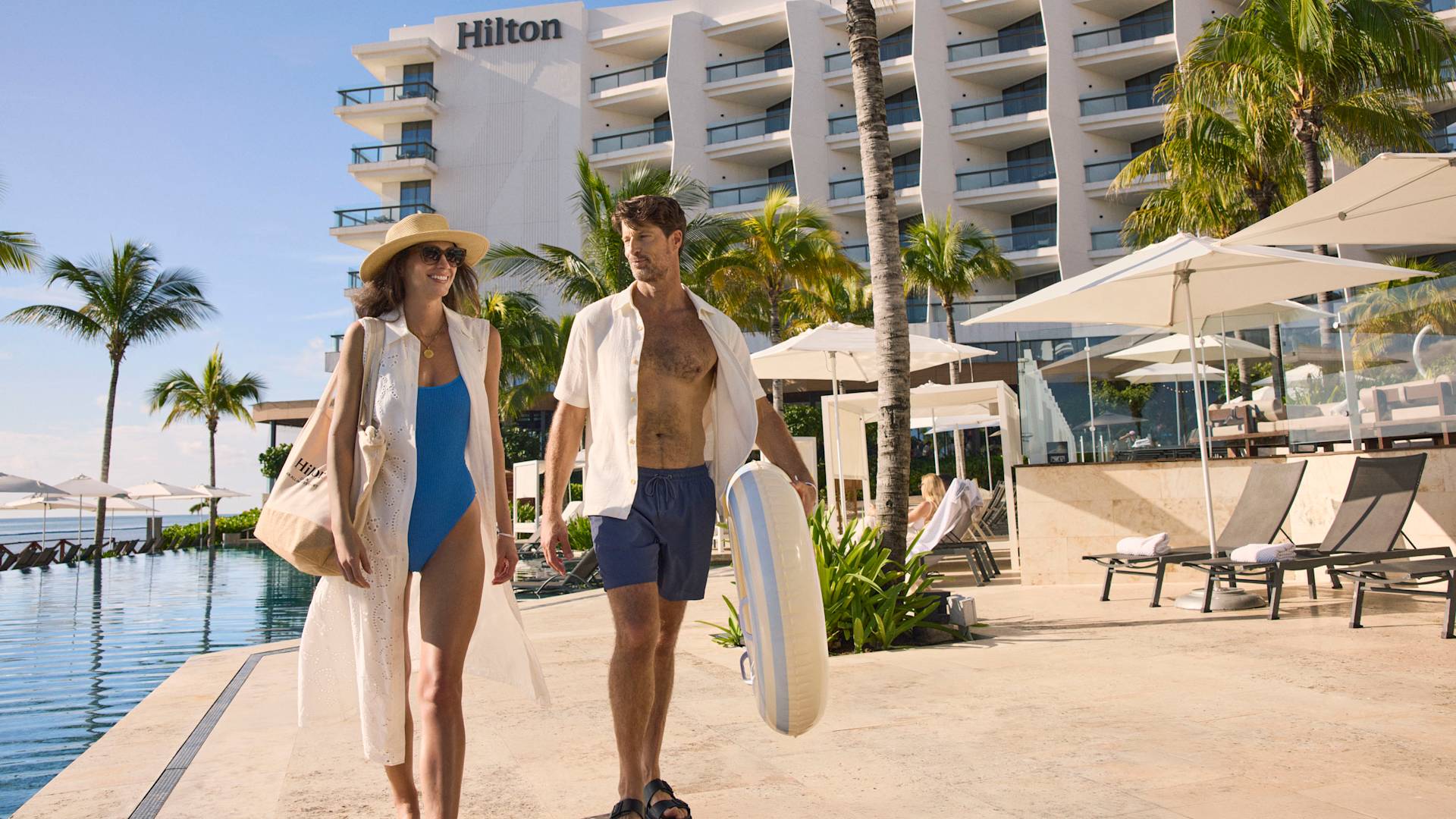 سيدة ورجل يسيران بجوار بحمام سباحة خارجي ويظهر الفندق في خلفيتهما