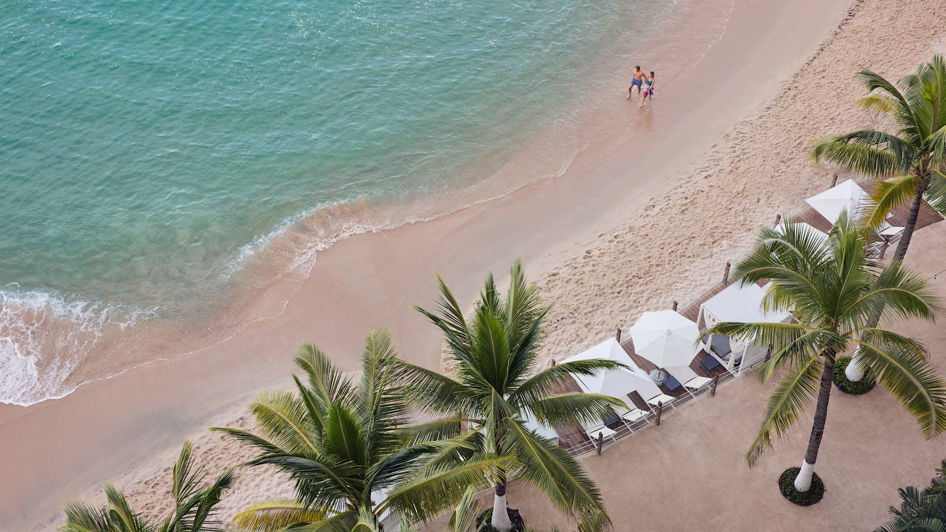 Un homme et une femme parlant à pied sur la plage après des palmiers et des cabanas