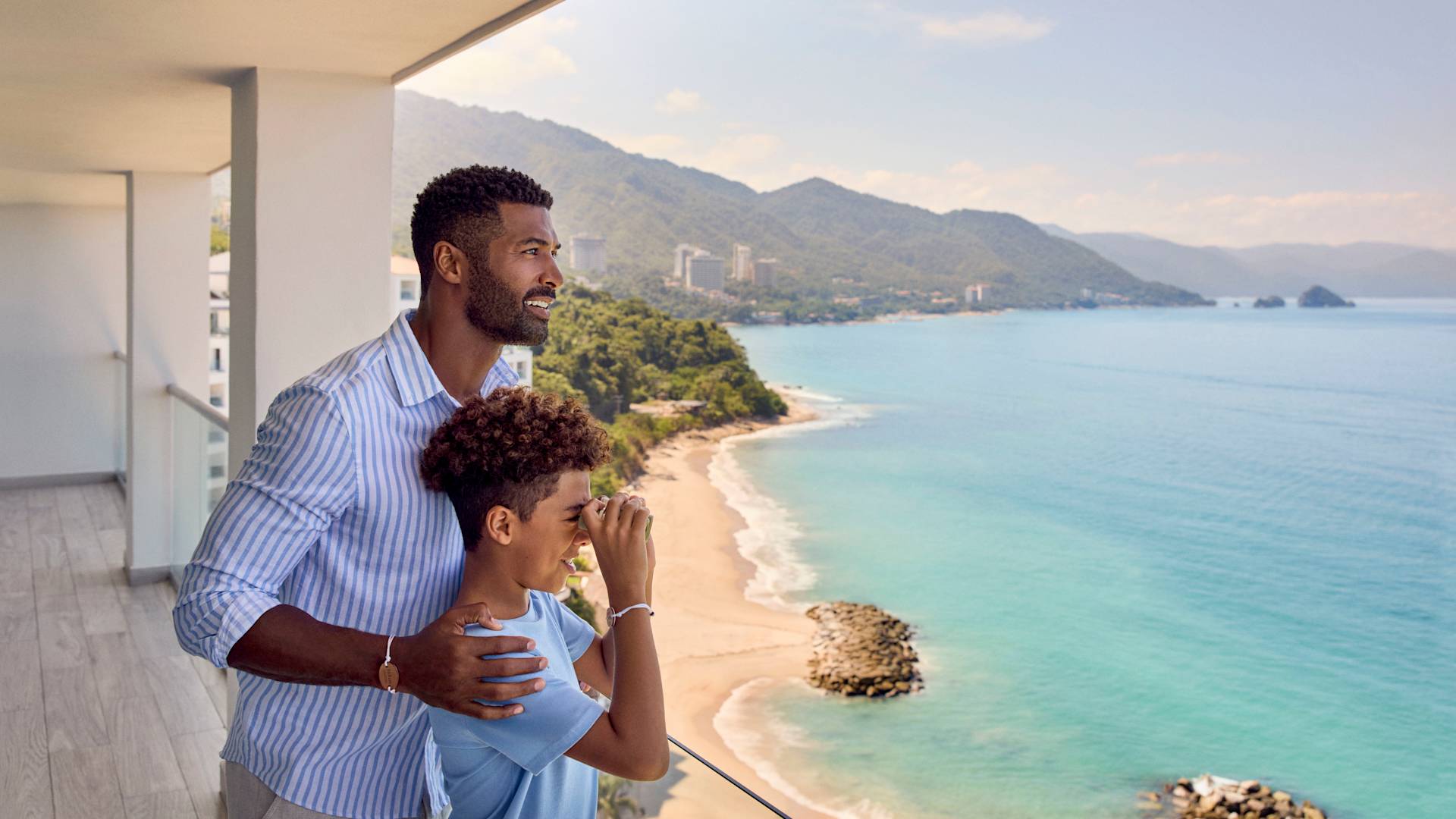 スイートのバルコニーに立って、双眼鏡で海を眺める父と息子