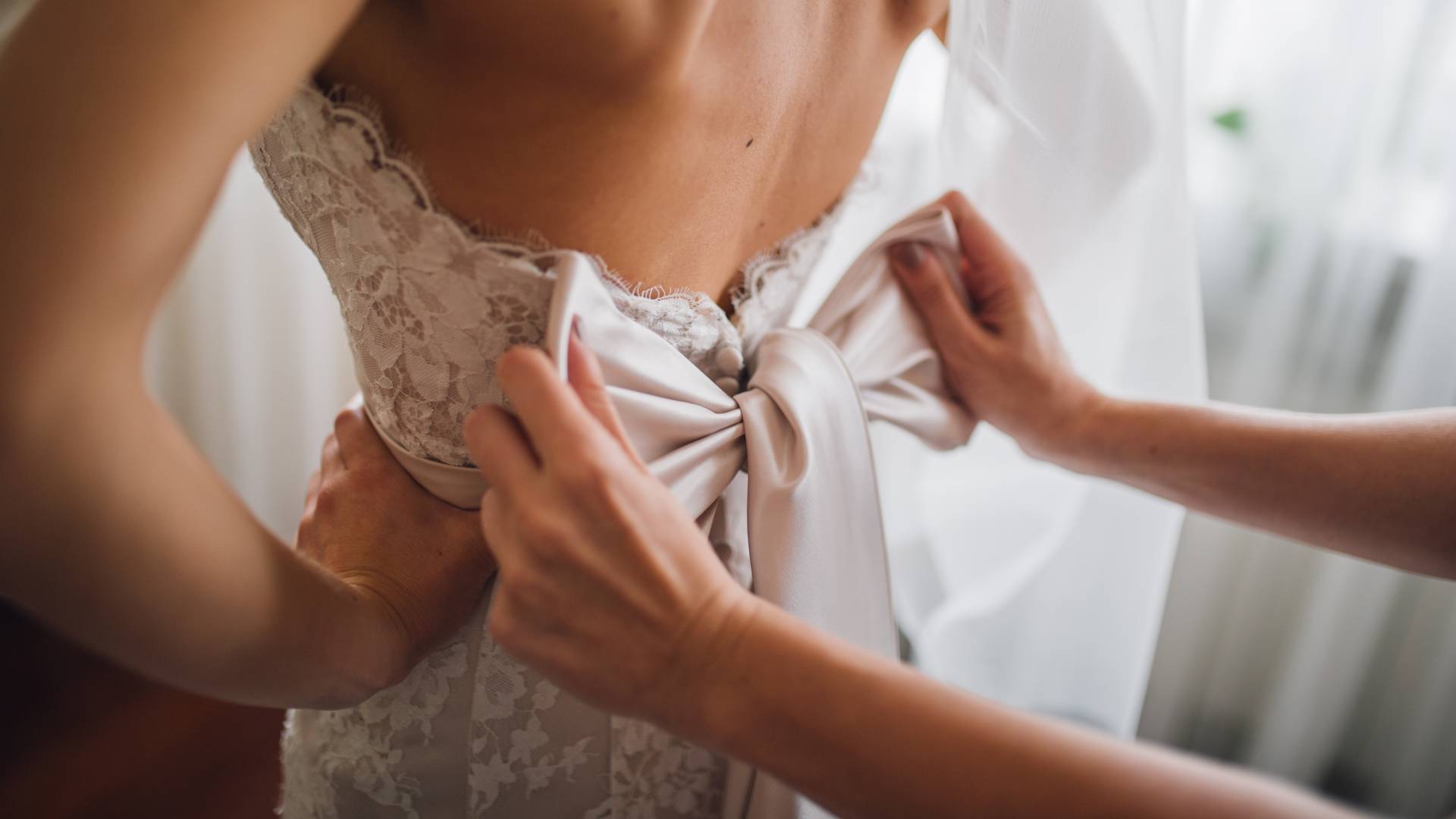 Bridesmaid makes bow-knot on the back of brides wedding dress