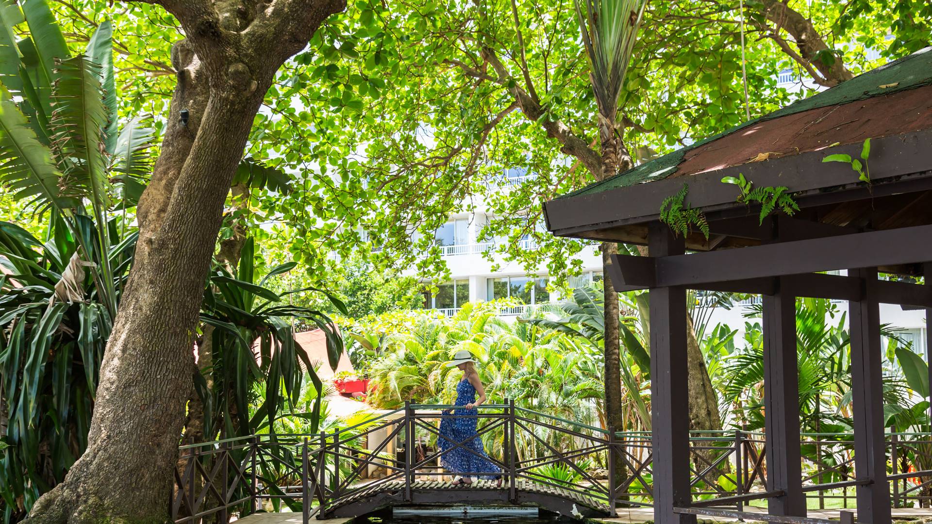 Mujer cruzando un puente en un jardín tropical