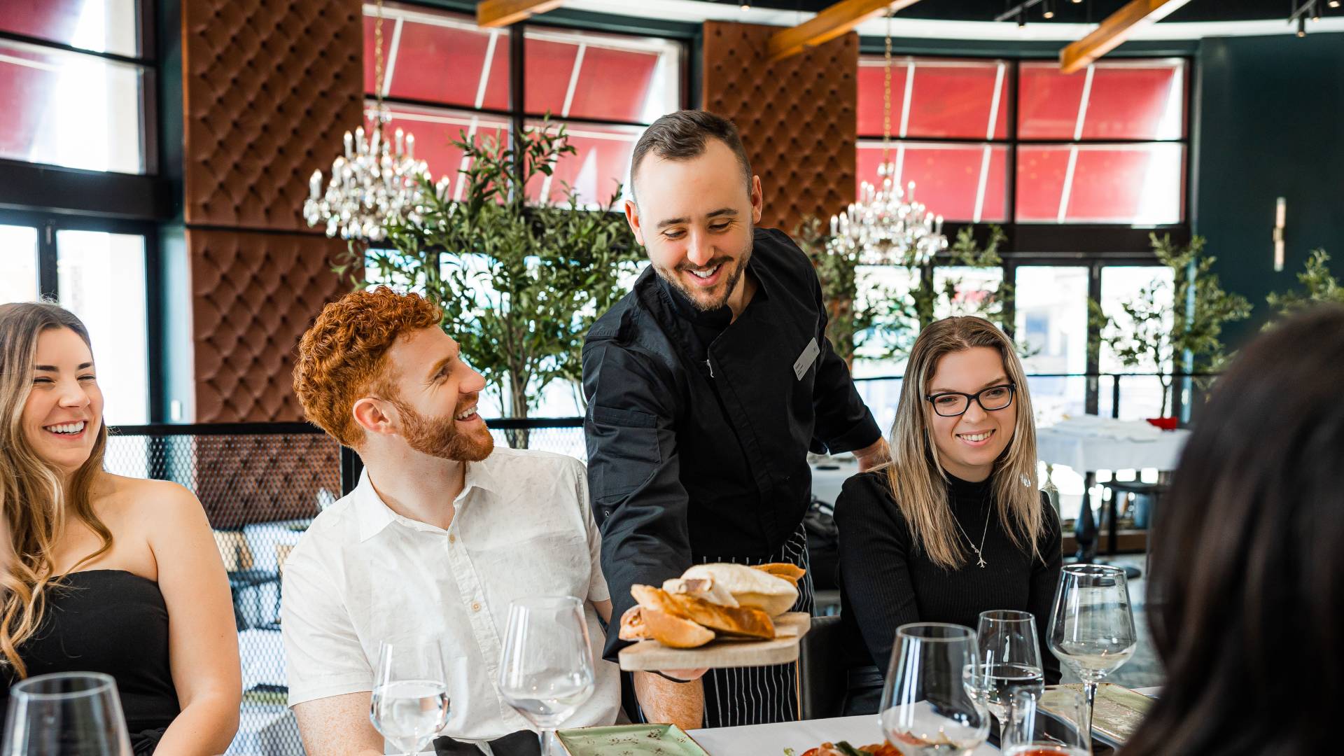 people sitting at dinner table and server placing bread on table