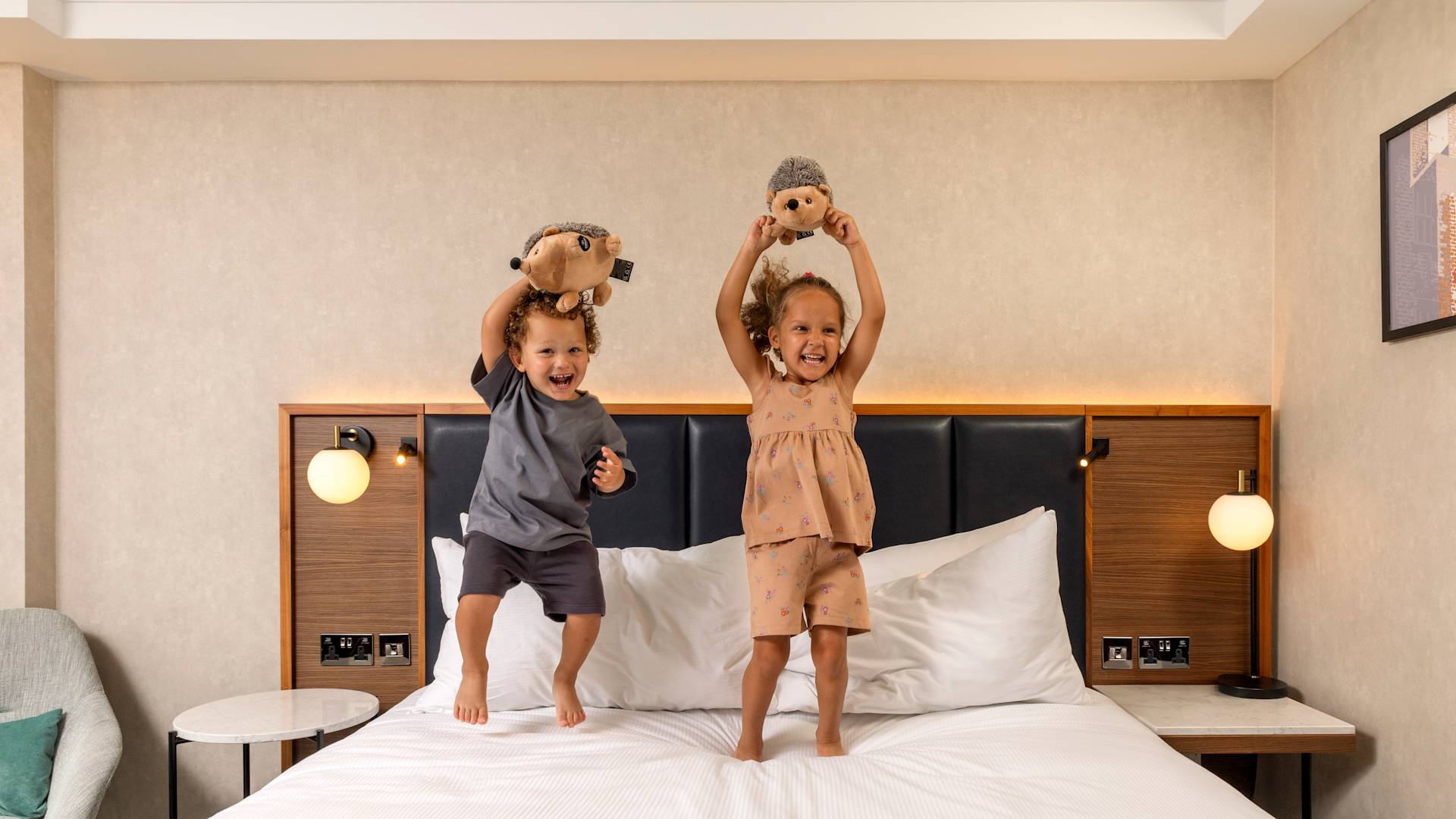 Kids Holding Stuffed Animals while Jumping on a Bed in a Guest Room