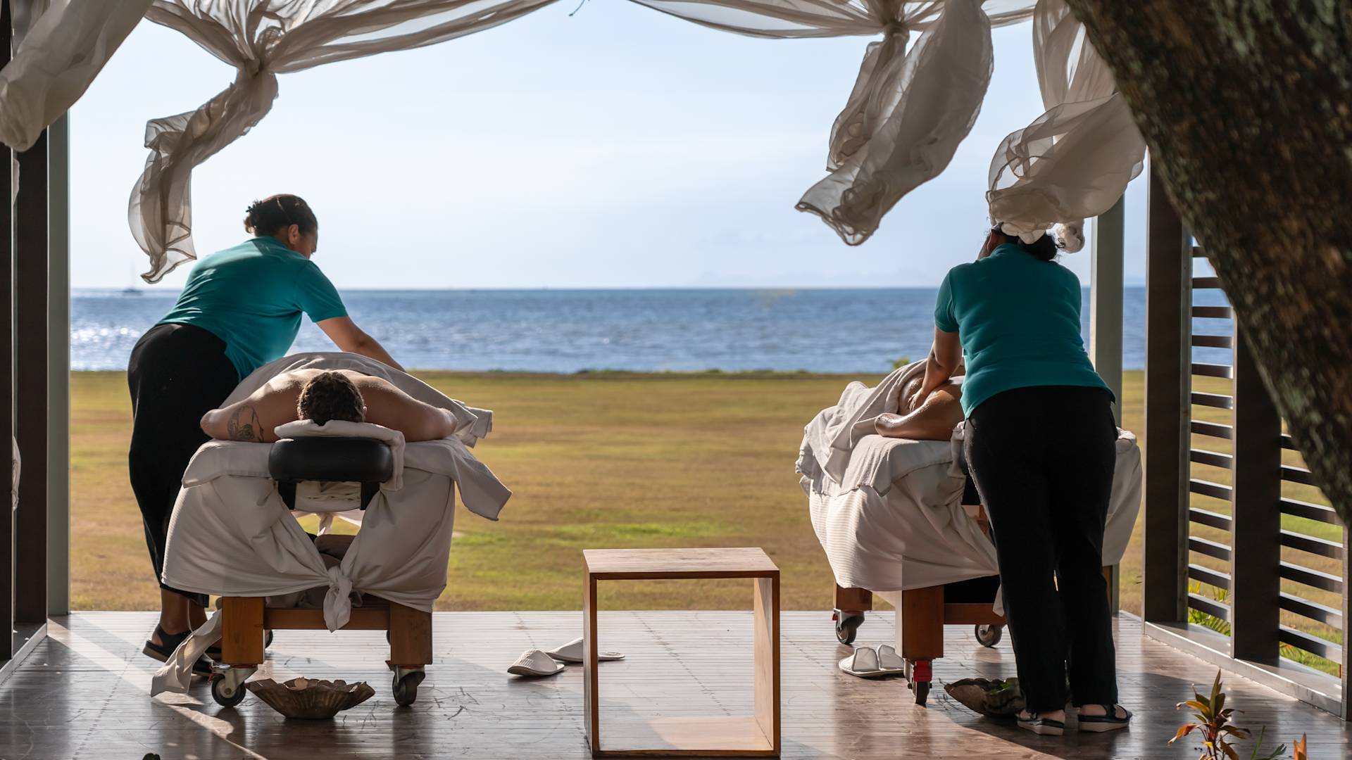 Two people receiving massages on massage tables, with view of sea