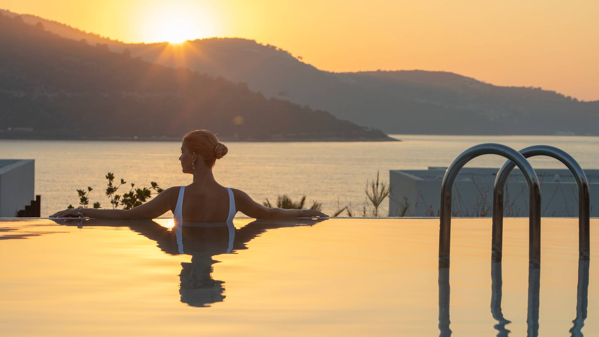 Havuzda denize ve gün batımına bakan mücevherli kadın