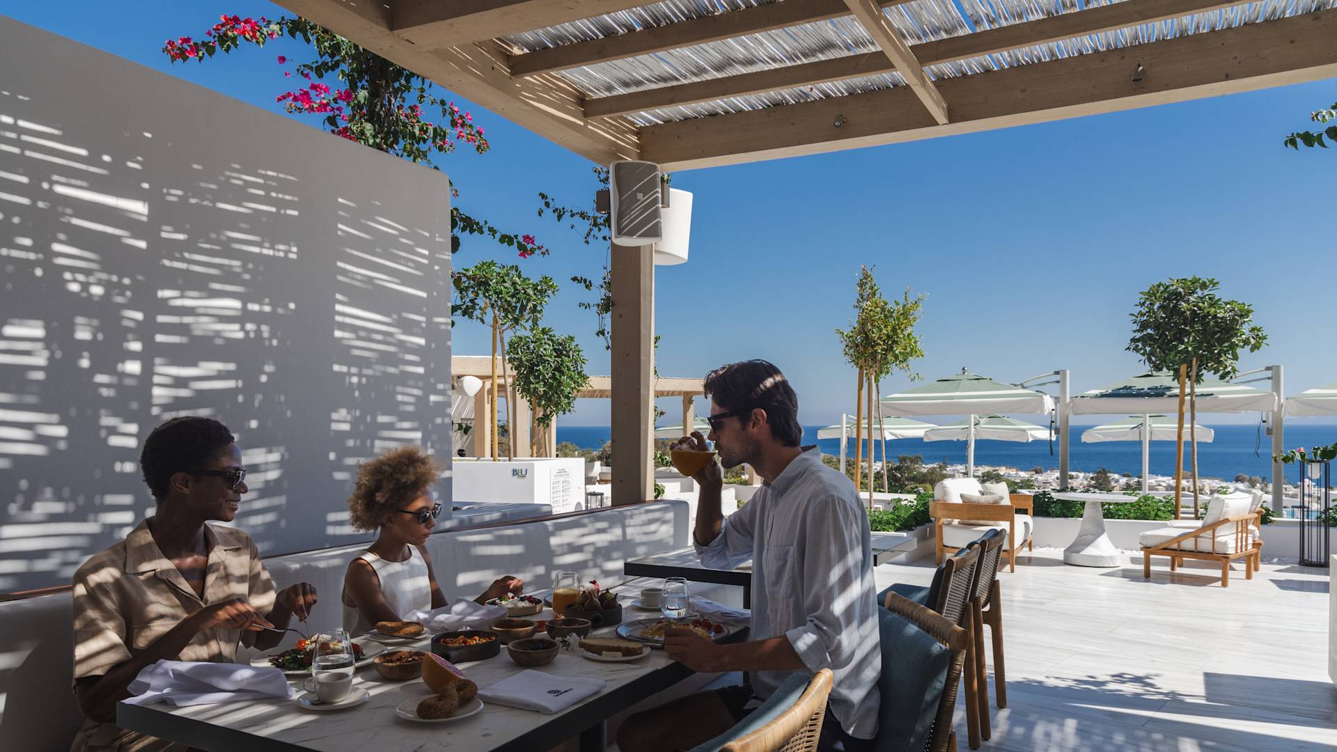 Dışarıda gölgede oturan, masada yemek yiyen aile