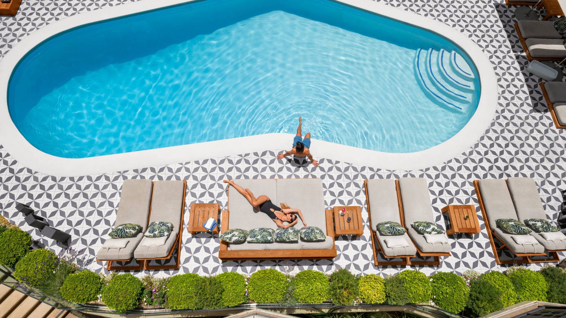 Wide aerial shot of woman sunbathing by pool with man sitting in pool