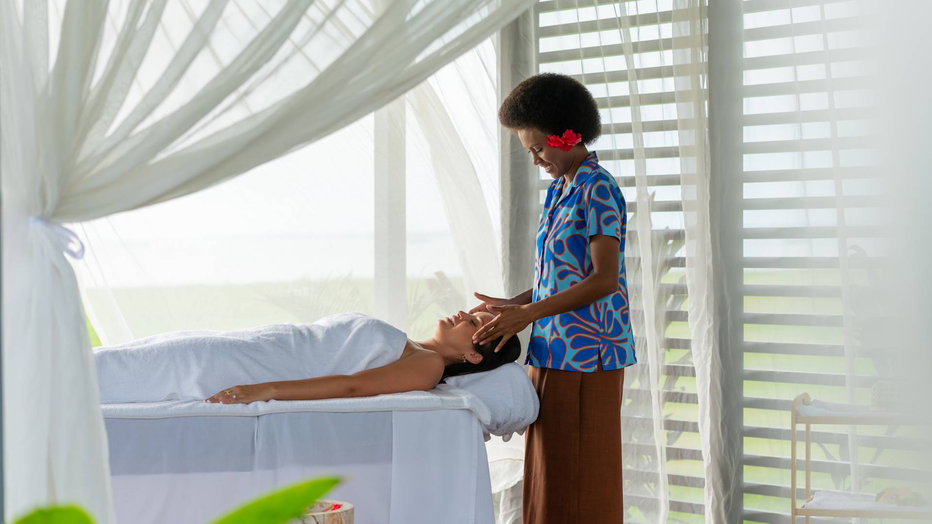 A female spa team member providing a massage to a woman under a flowing tent set up.