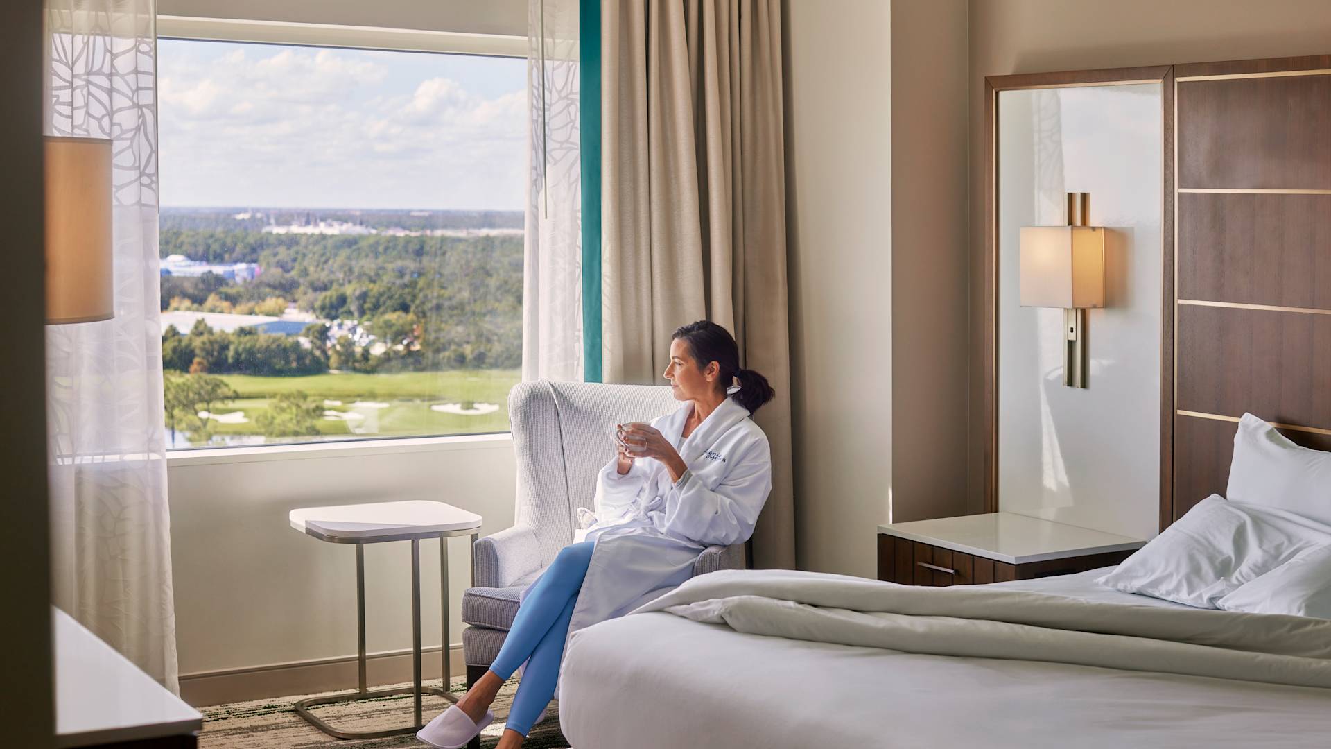 Femme se relaxant dans l'espace salon d'une chambre tenant une boisson