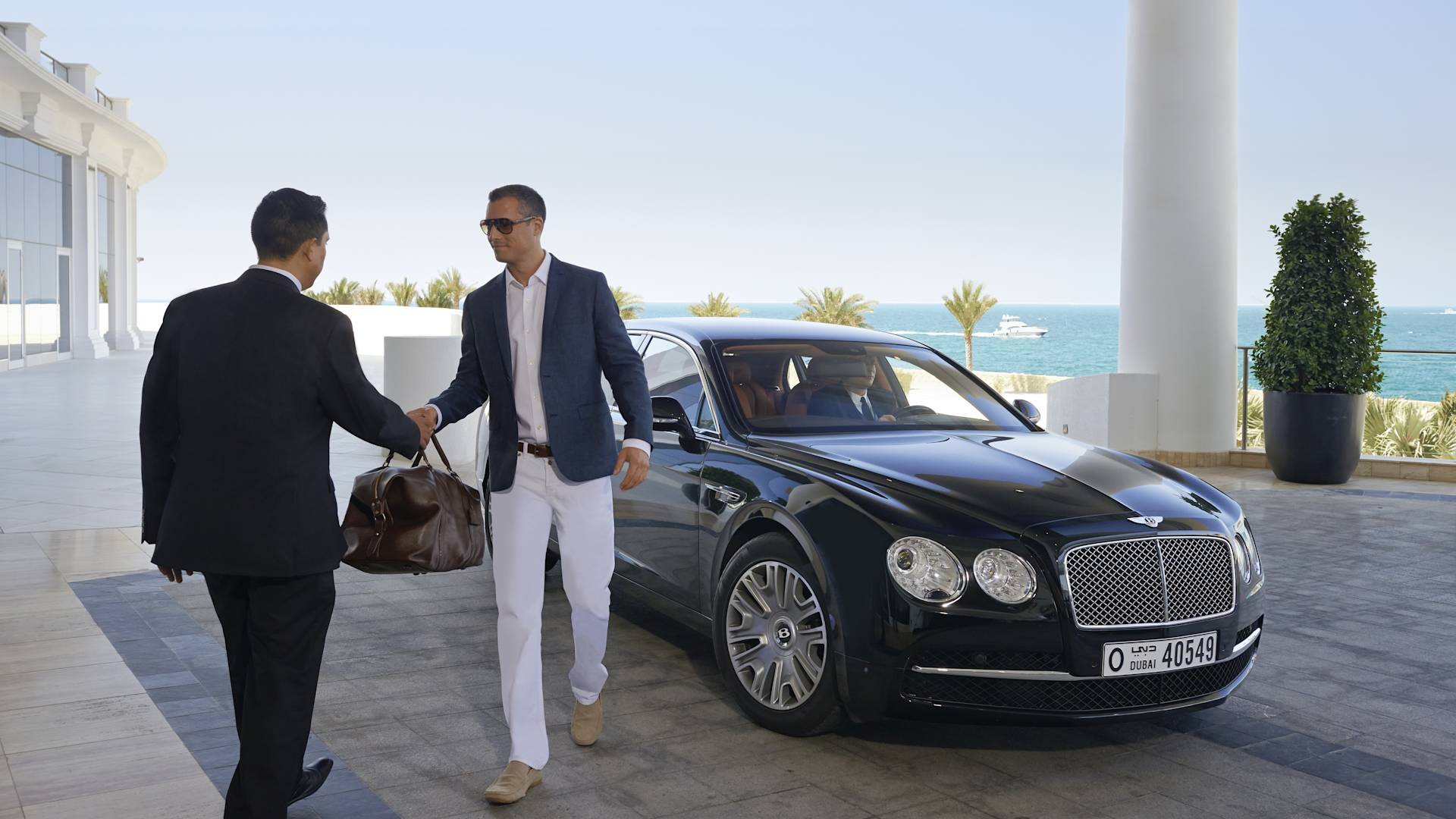 Pria keluar dari mobil dan menyerahkan tas ke portir di pintu masuk hotel