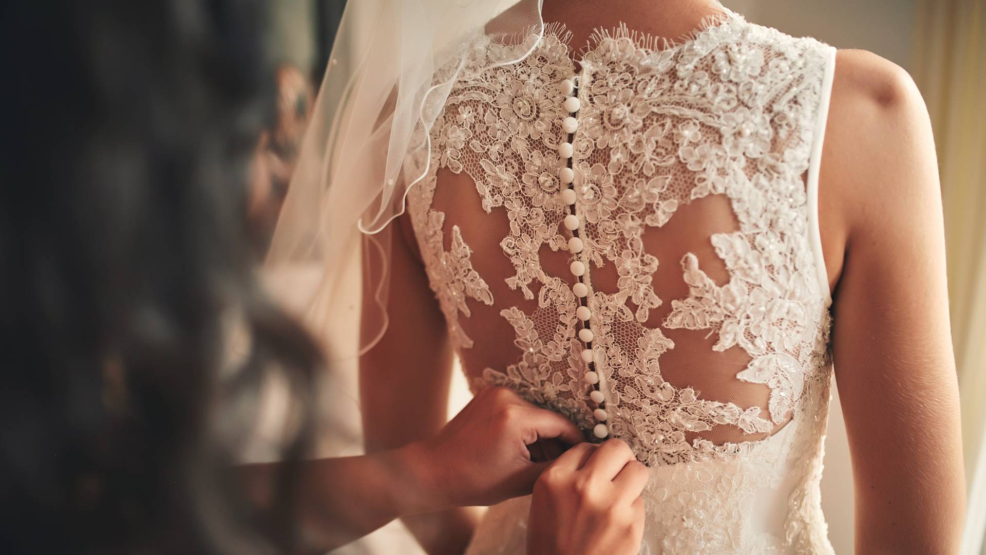 Bride having the back of her lace wedding dress buttoned up