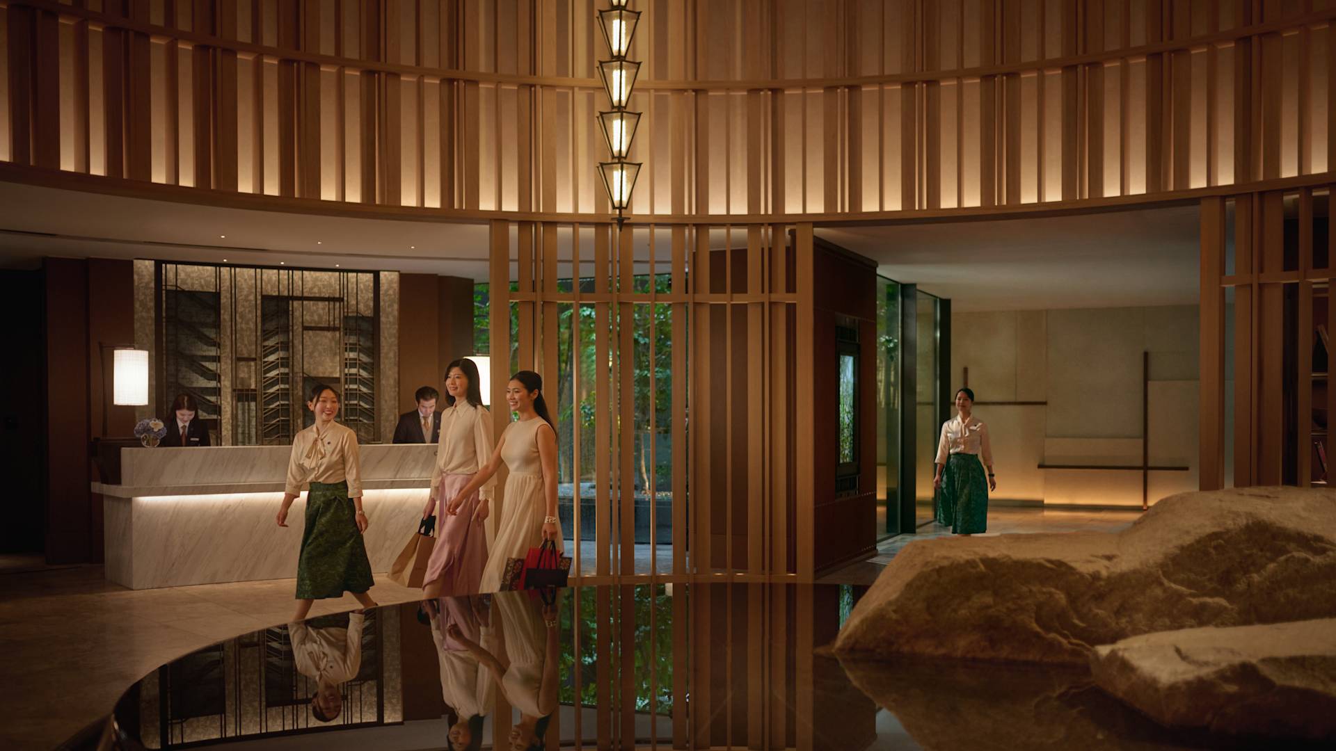 ロビーで女性のお客様をご案内するコンシェルジュと、フロントデスクに常駐するホテルのチームメンバー。