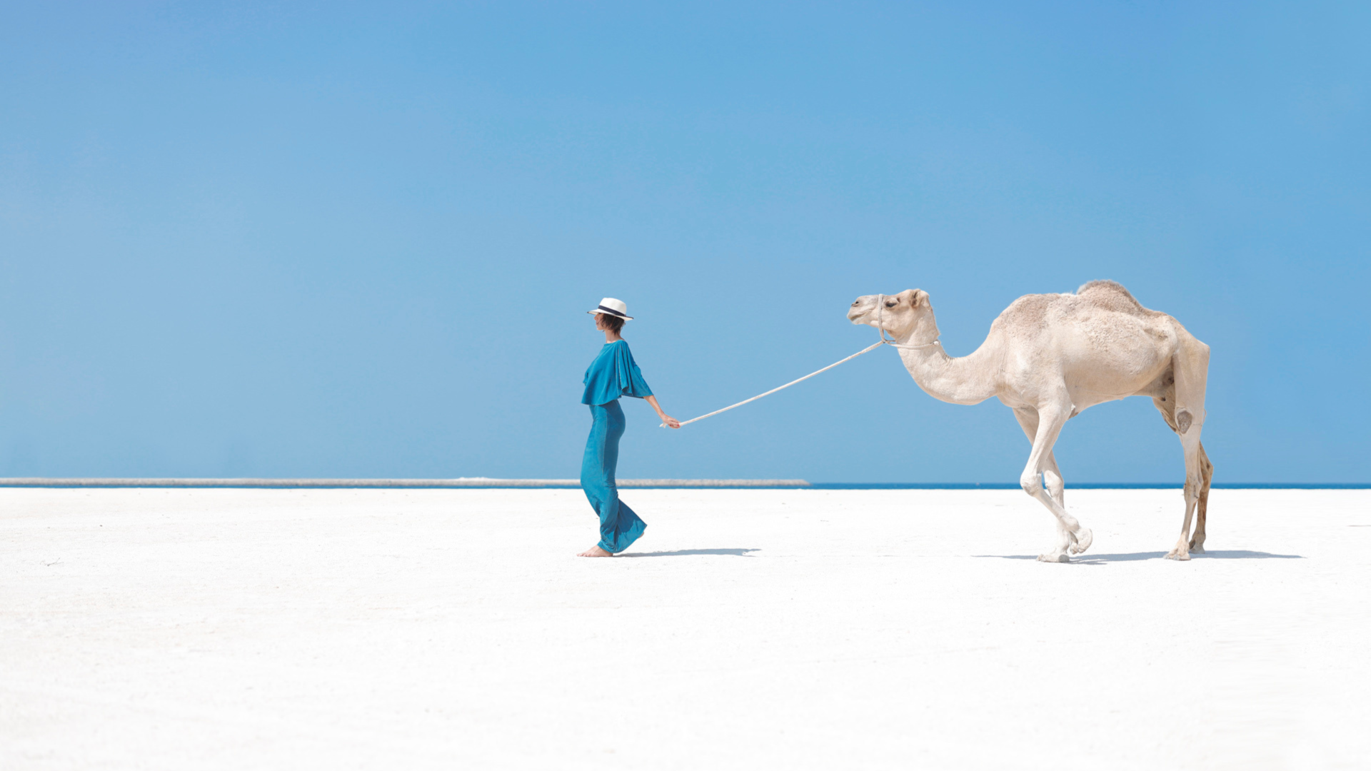 a lady leading a camel in the desert