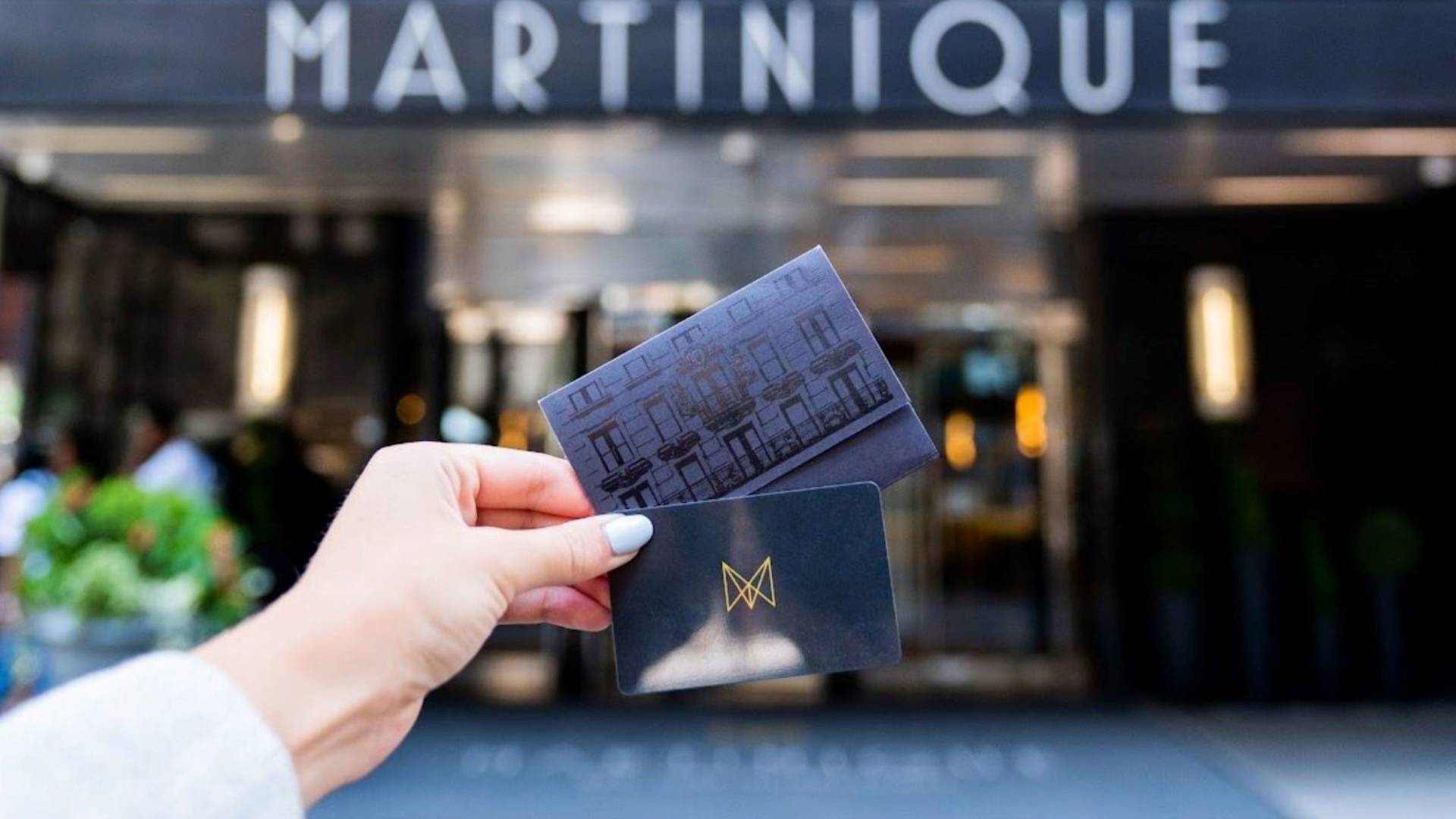 Hand holding Martinique card in front of hotel entrance