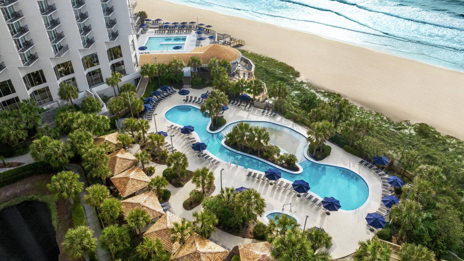 Aerial view of stunning oceanside hotel with pool and beach.