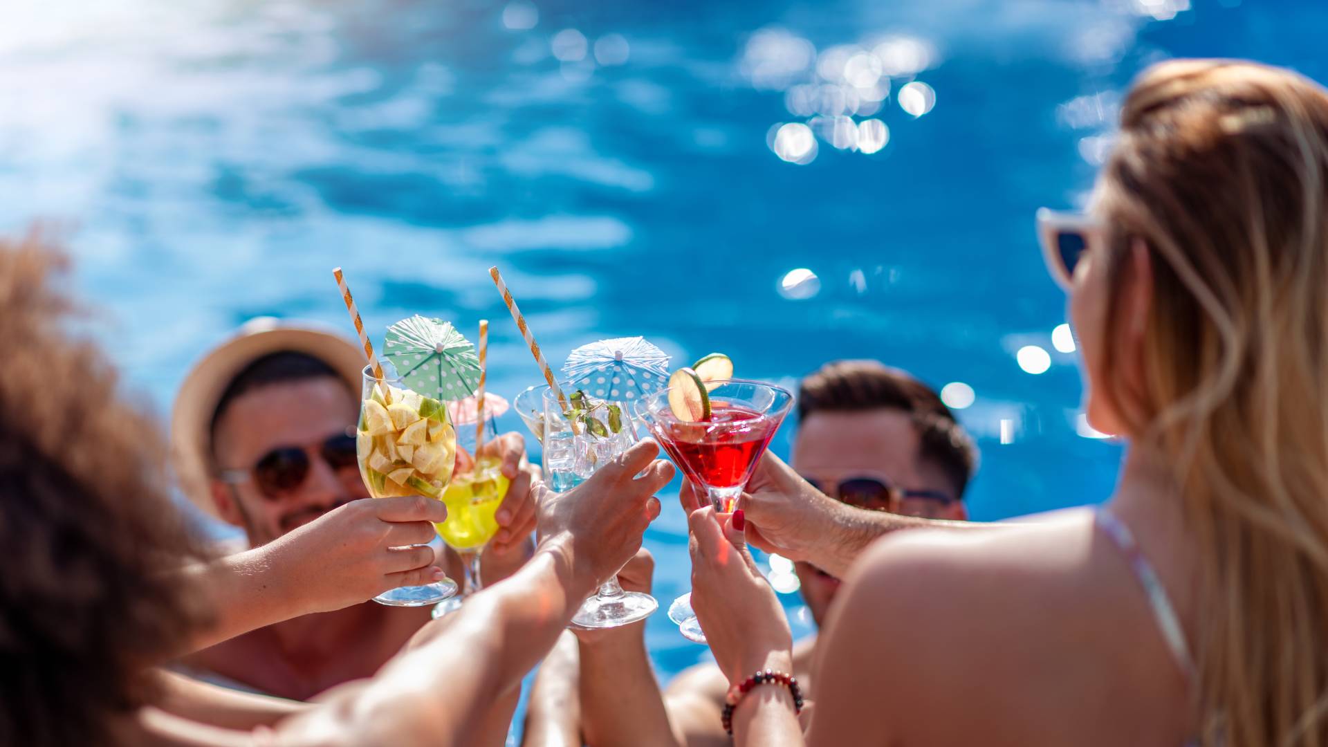 Des personnes au bord d'une piscine toastant avec des cocktails