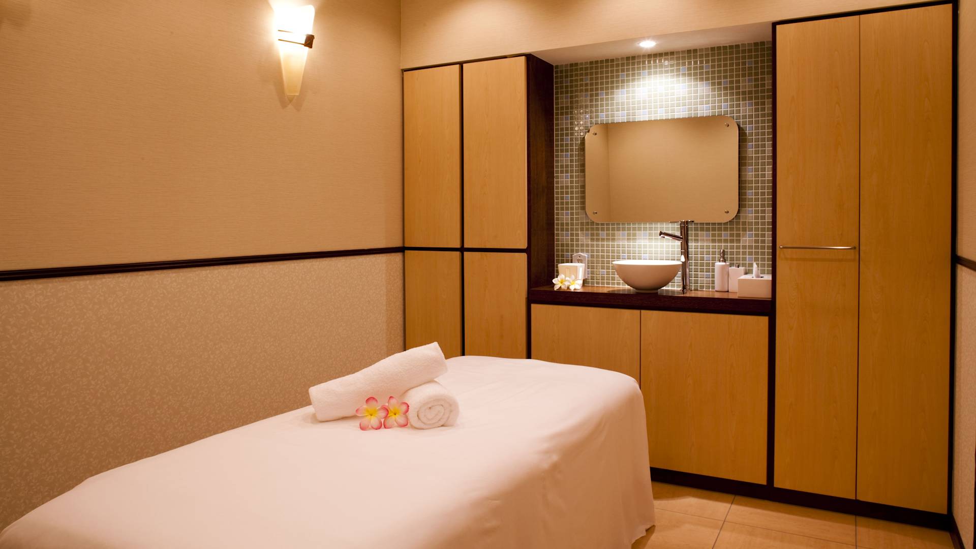 Salón de relajación con flores y toallas sobre mesa de masajes y lavamanos