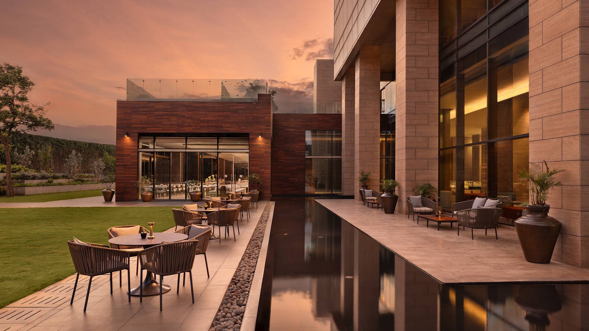 Outdoor patio with tables and chairs beside a reflecting pool and lawn at dusk.