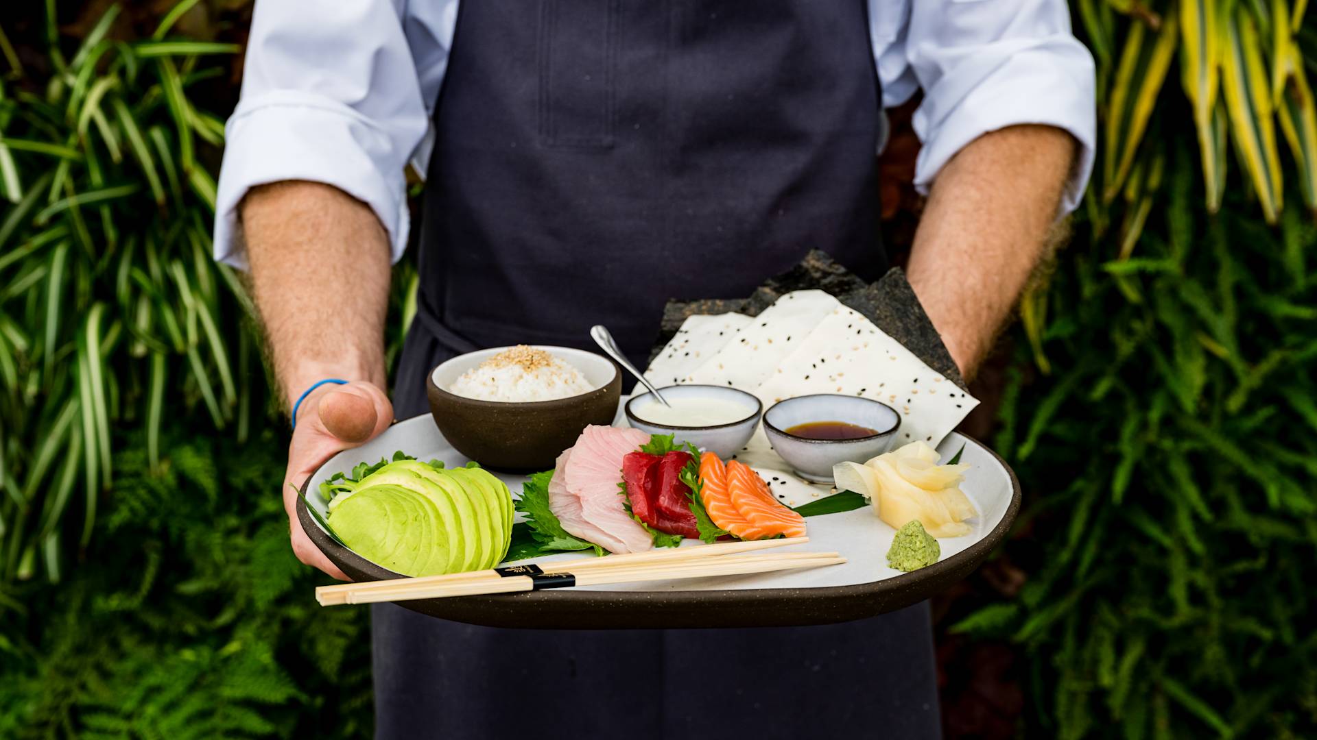 Plate of asian inspired food including fish an dipping sauce, rice and avocado. Plate is held by a server.