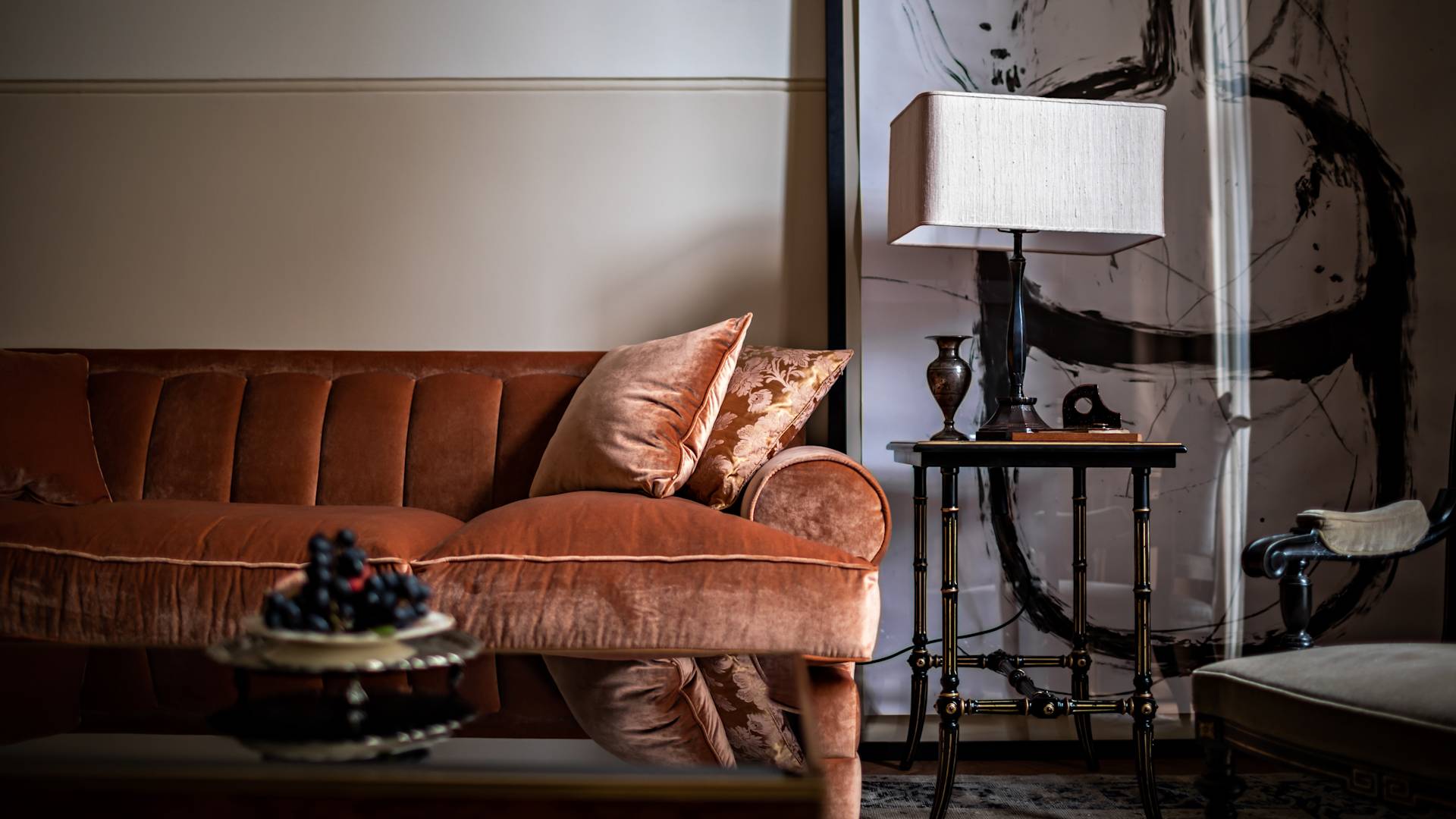 Living room with a brown velvet sofa, side table with lamp, and an abstract painting on the wall