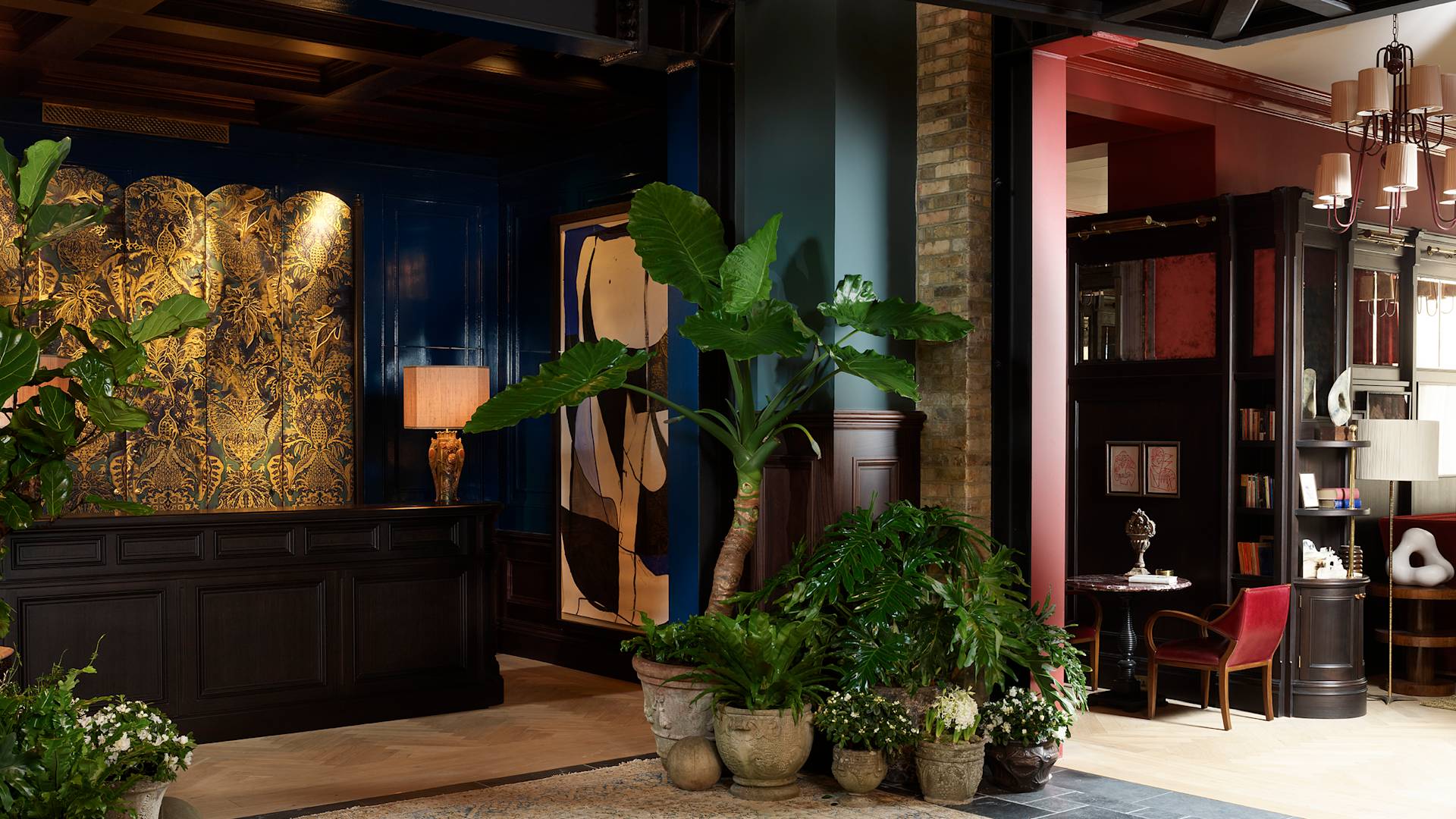 A lobby area with a dark reception desk, large potted plants, a blue wall with artwork, and a cozy seating nook.