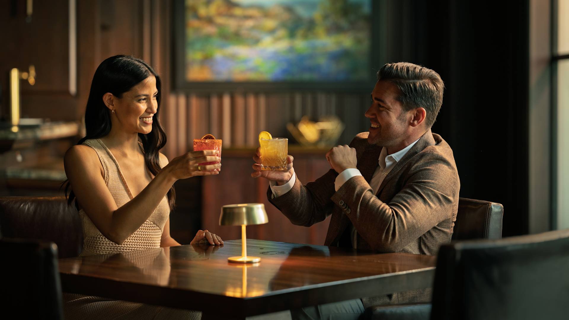 A man and woman toasting with cocktails at the bar