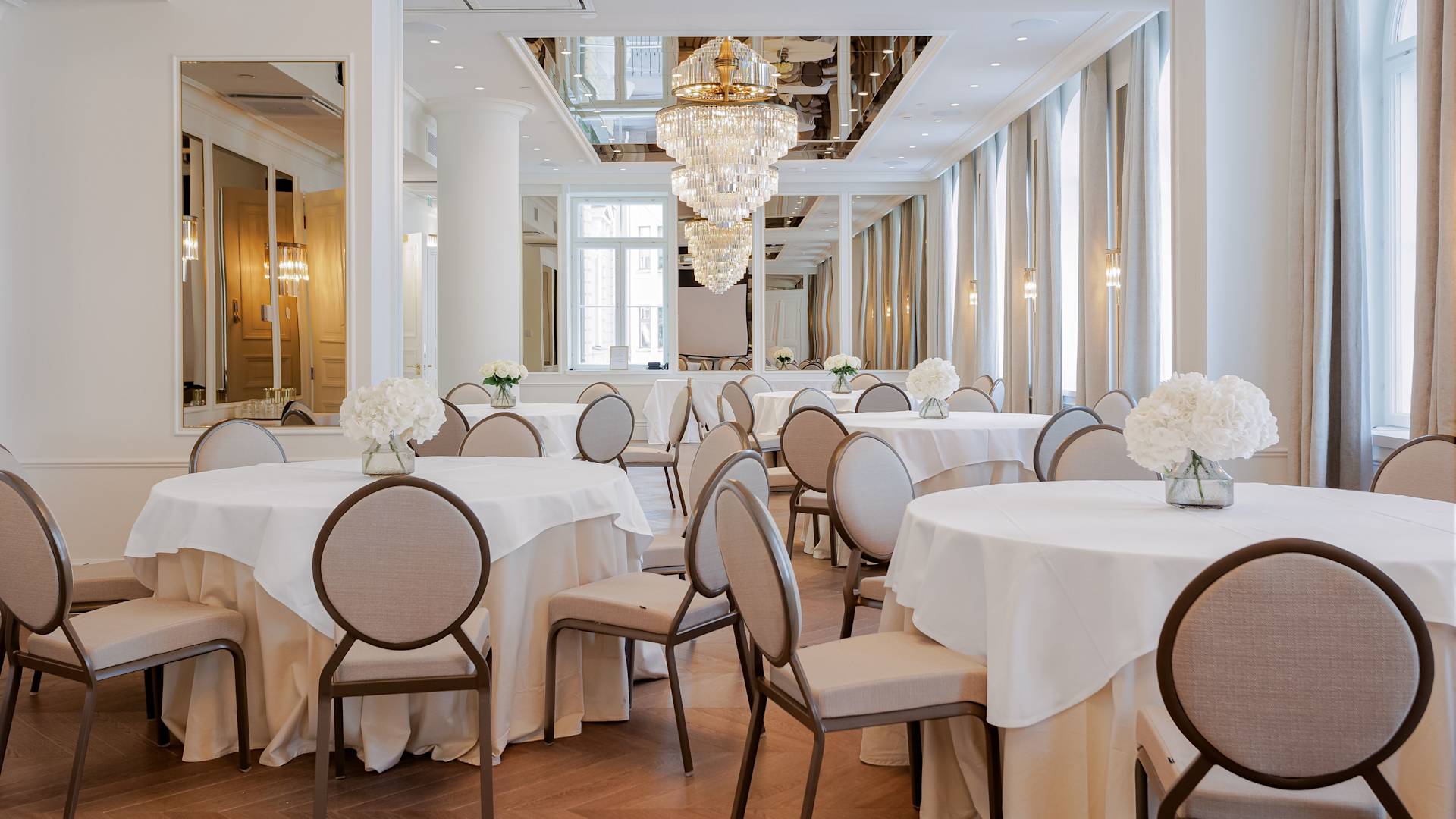Salón de fiestas con mesas redondas, arreglos florales y chandeliers