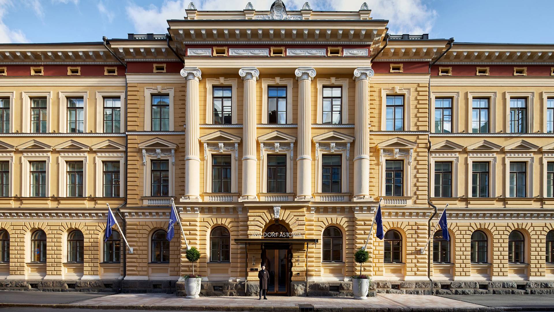 Eksterior hotel dengan porter di depan pada hari yang cerah