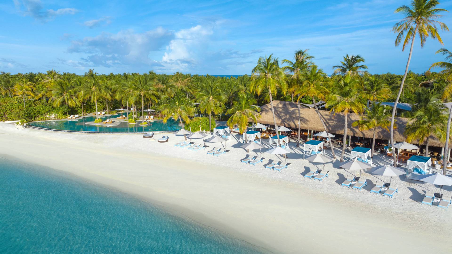 Blick auf den Strand von Nava mit Loungesesseln und Palmen