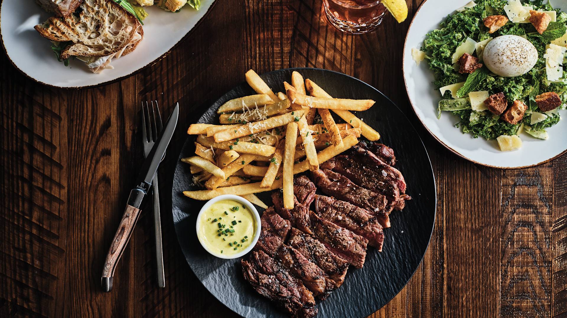 Meat with Sauce and Fries on a Plate, Salad and a Drinks on a Table at Powder Restaurant