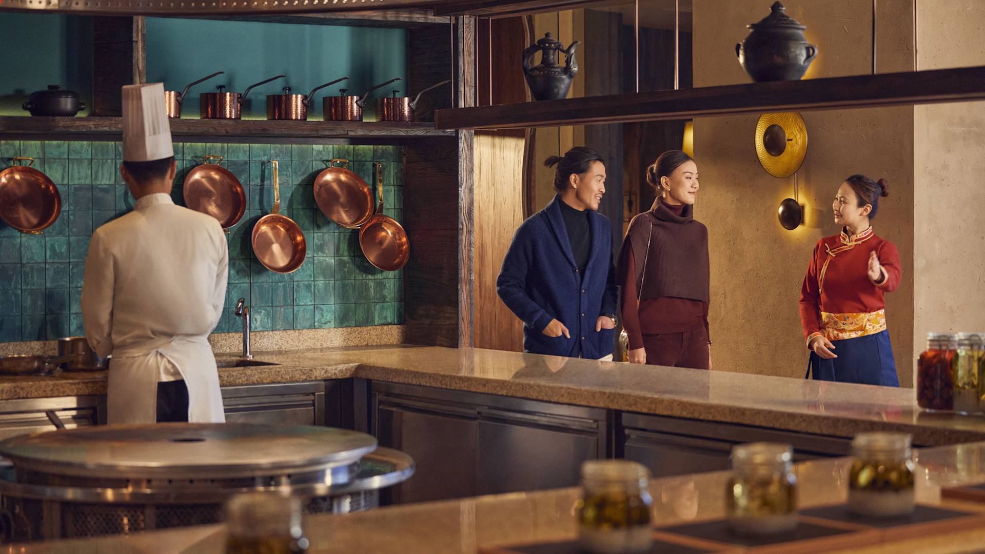 Pria dan wanita berjalan melalui restoran dipandu oleh anggota staf sebagai koki yang bekerja di transisi