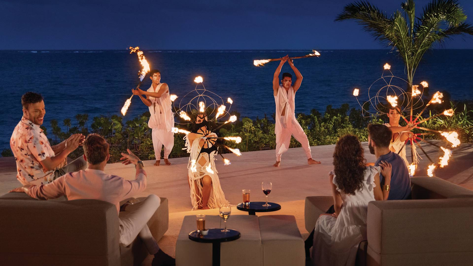 Guests watch and cheer for fire dancers in front of the ocean-transition