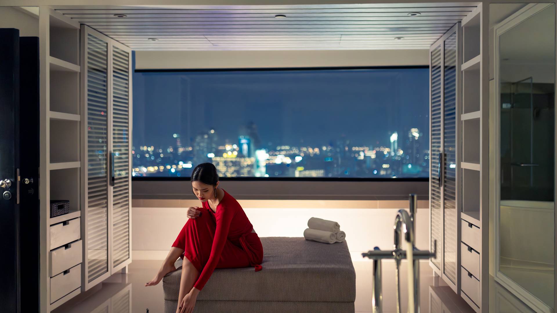 Femme se préparant à sortir dans une suite avec vue sur la ville la nuit, en transition