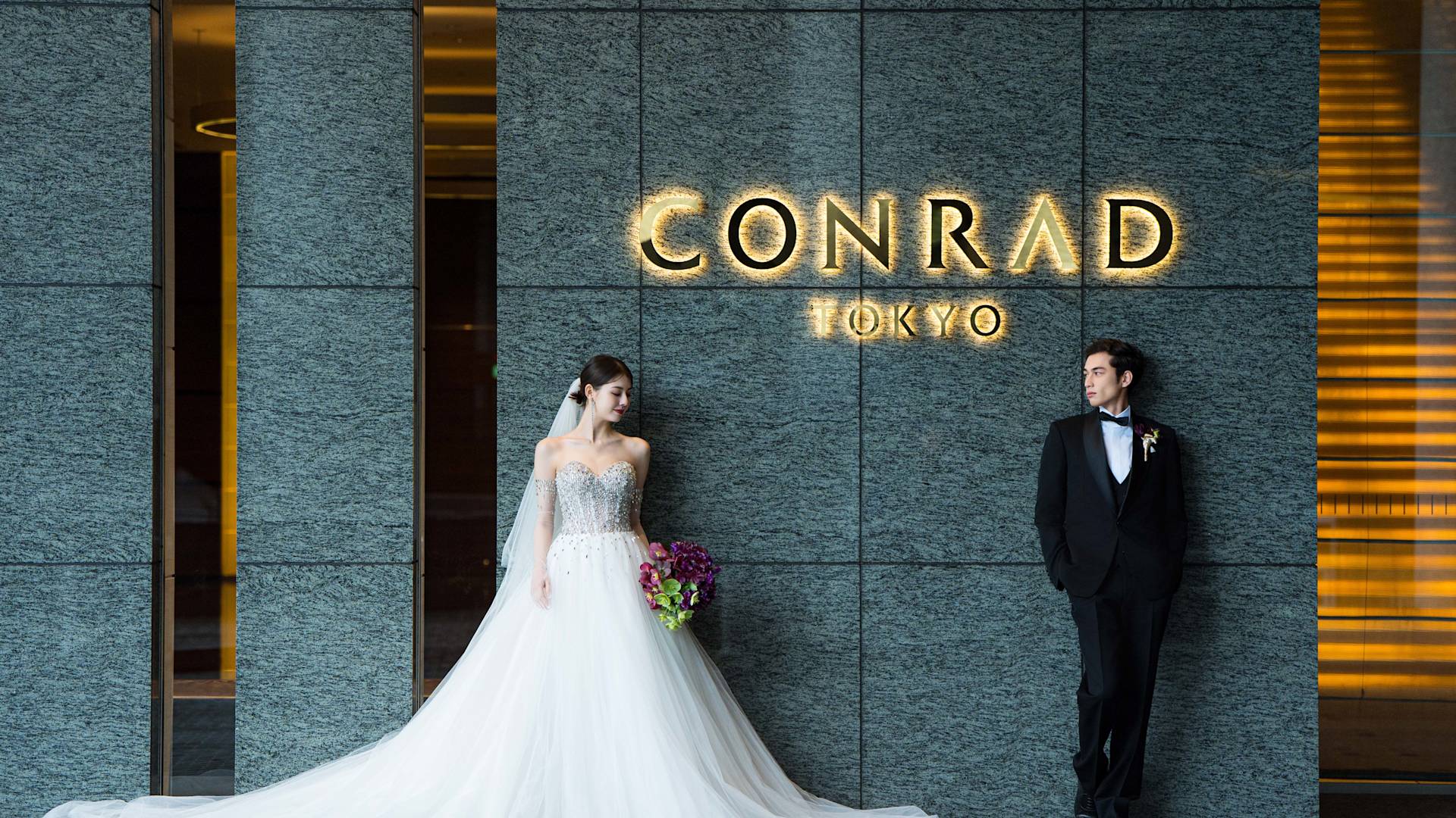 Un couple dans un smoking et une robe de mariée pose devant l'hôtel Conrad Tokyo - Transition